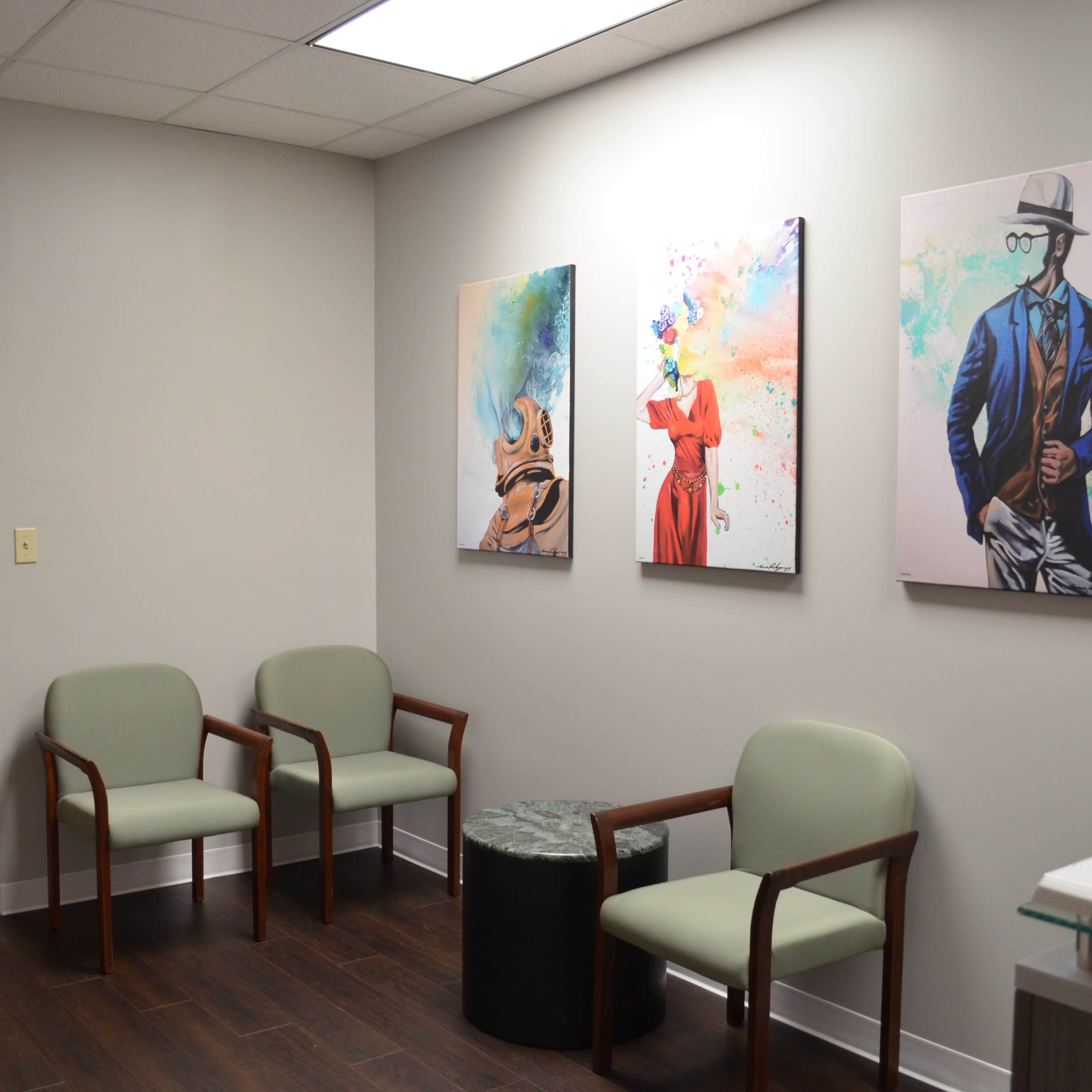 A waiting area features two green chairs, a small black table, and three colorful art pieces on the wall.