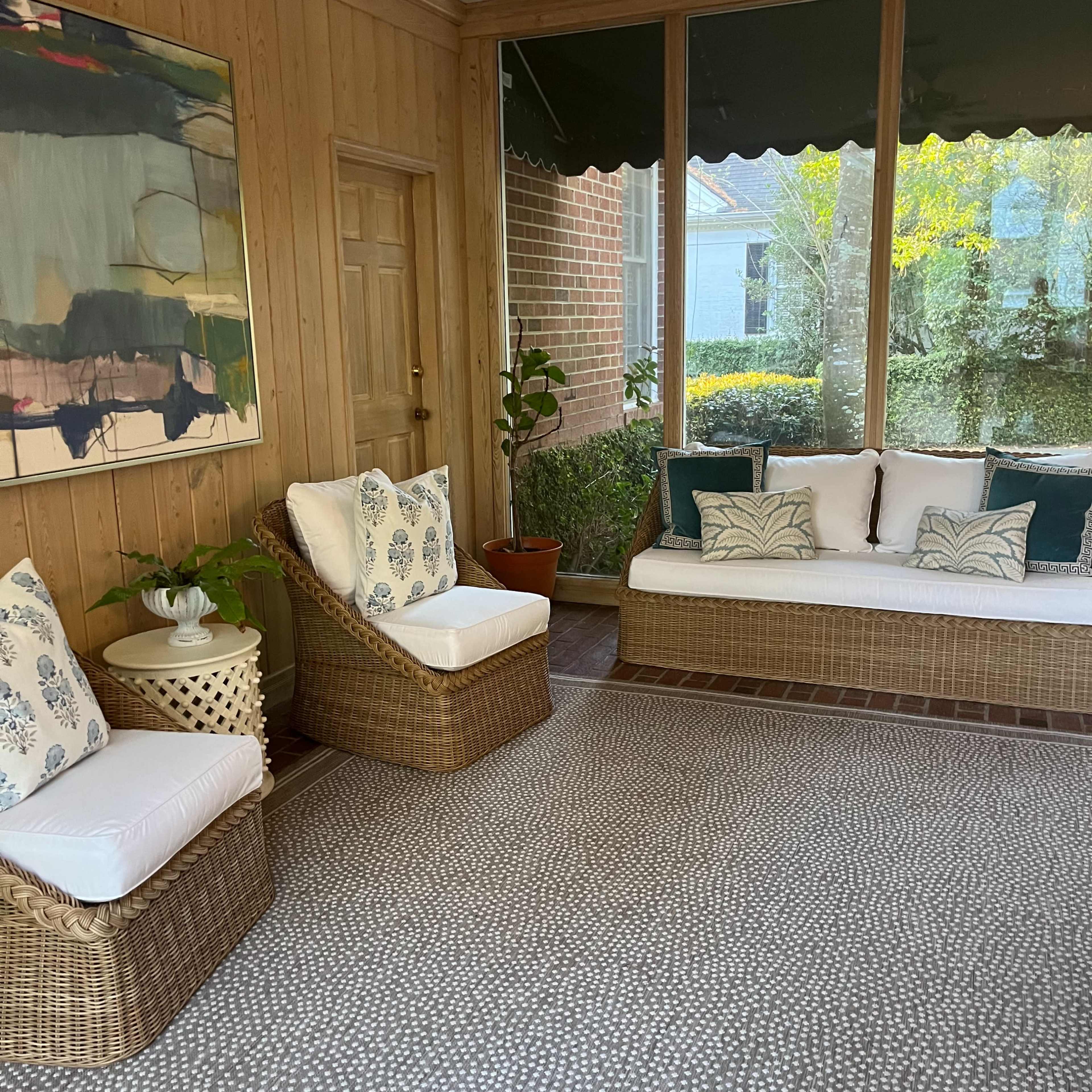 A sunroom with wicker seating, a large abstract painting on the wall, and a patterned rug.