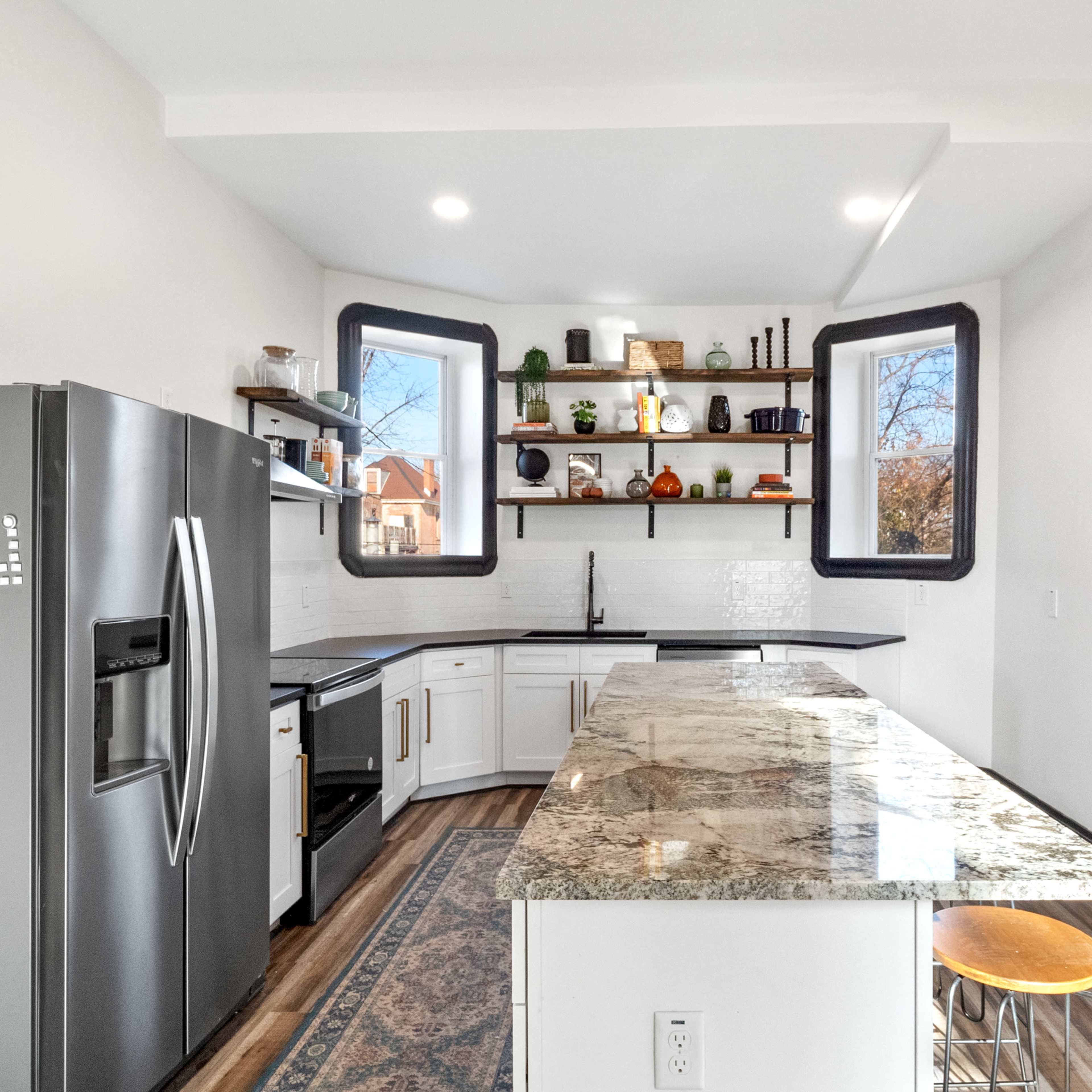 A modern kitchen features stainless steel appliances, white cabinets, and a large granite countertop with shelves displaying various kitchen items.