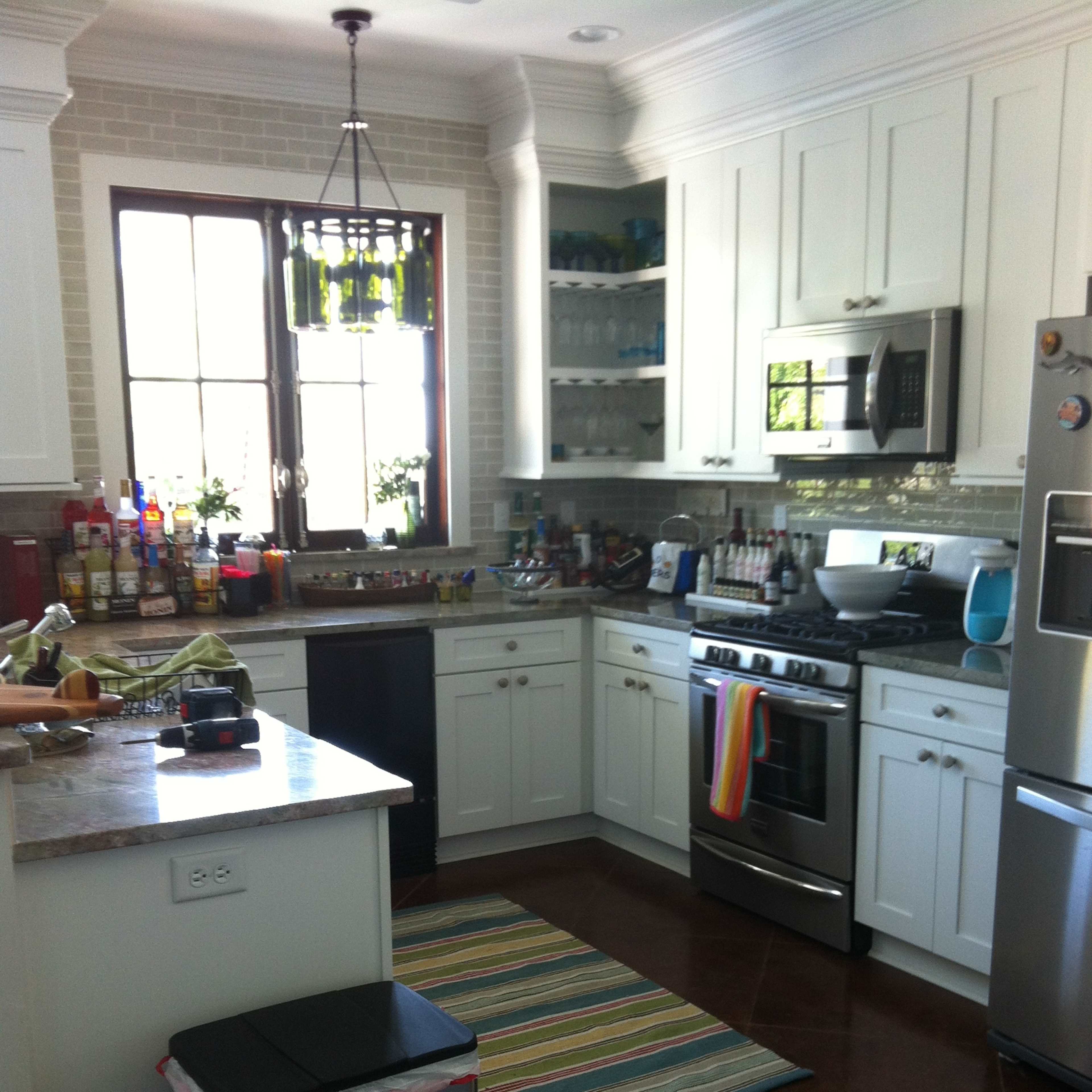 A modern kitchen features white cabinetry, stainless steel appliances, a striped rug, and a window allowing natural light.