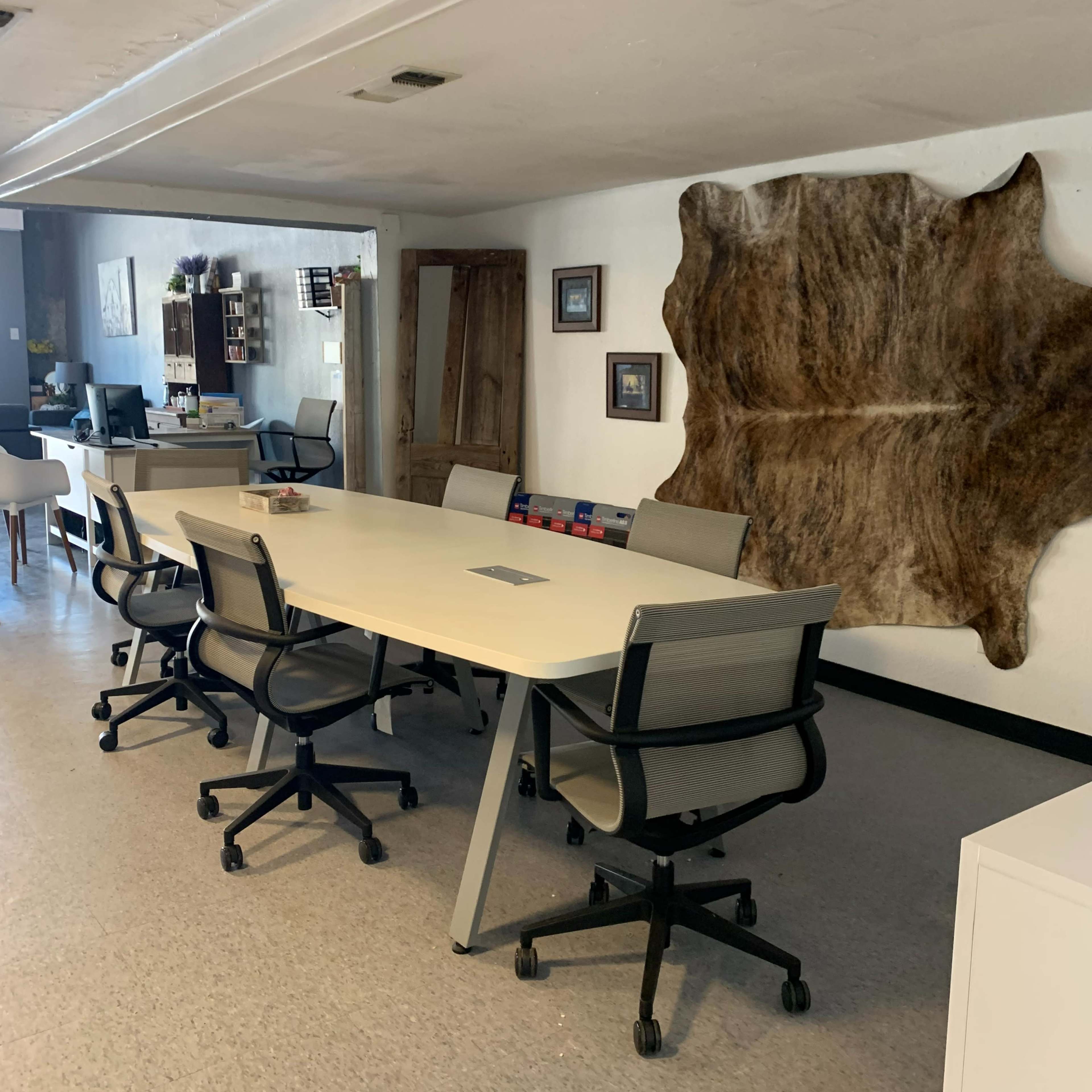 A spacious conference room with a long white table surrounded by rolling chairs and a decorative hide on the wall.
