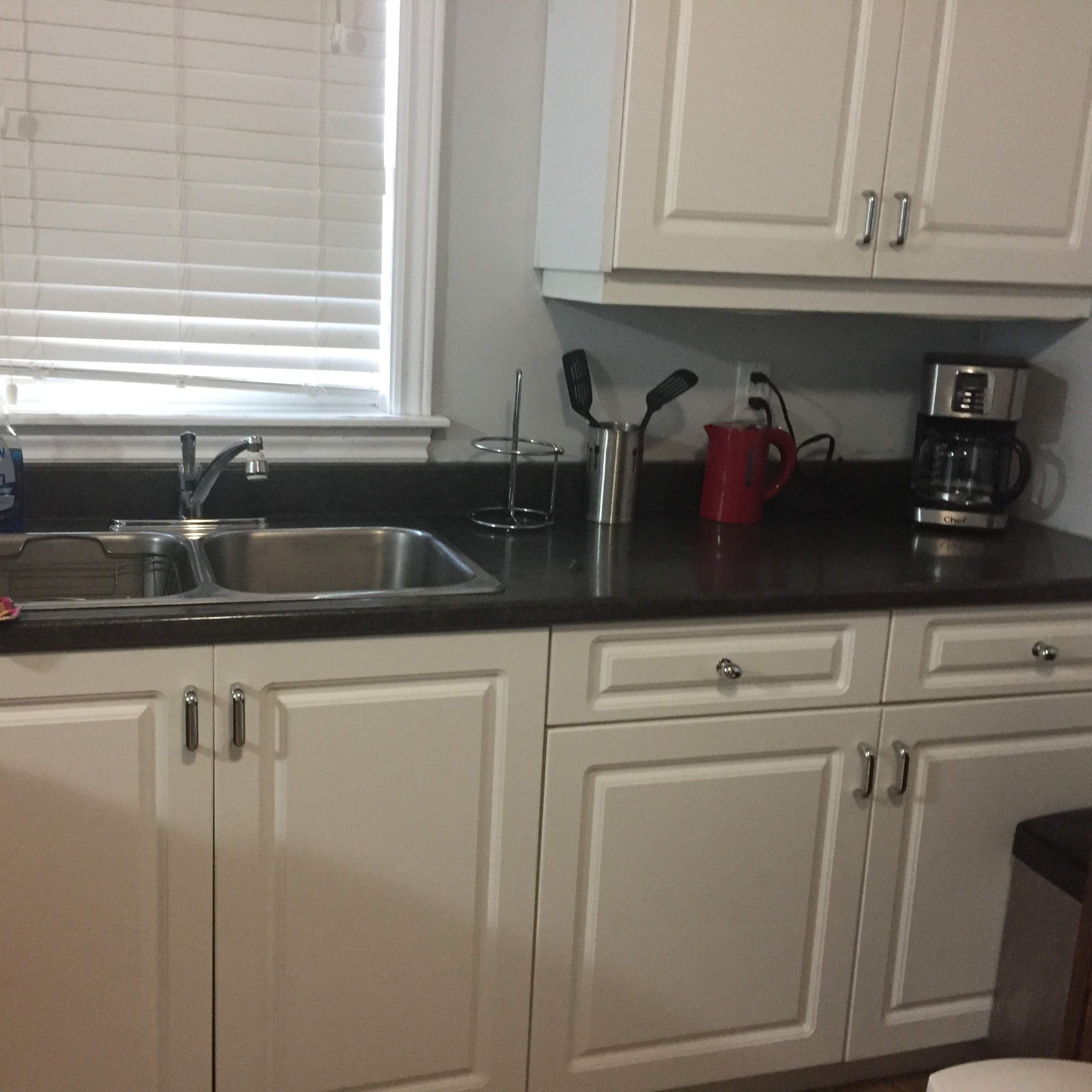 A kitchen countertop with a sink, a coffee maker, a red kettle, and kitchen utensils organized in a holder.