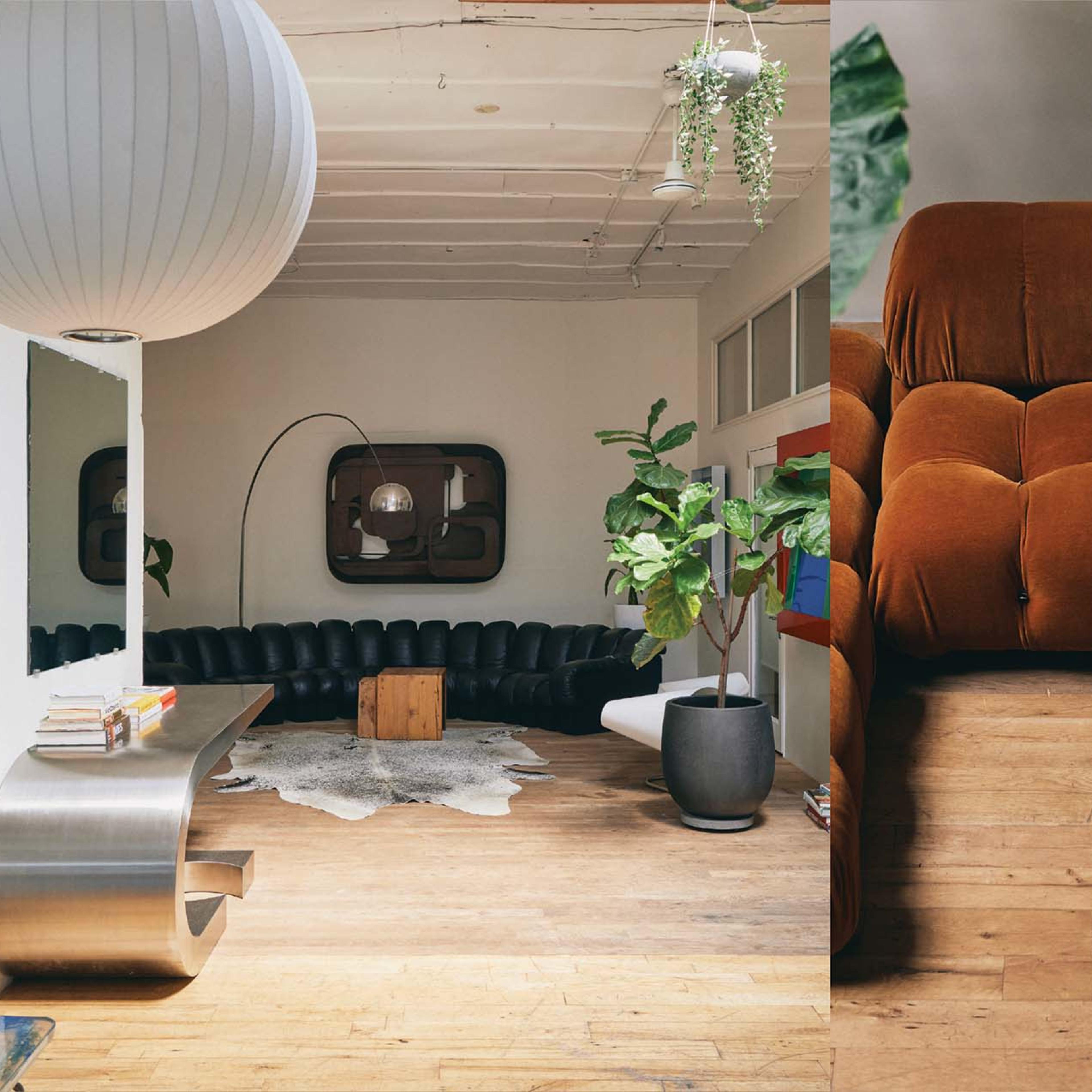 A spacious room with modern furniture, featuring a large black sectional sofa, a wooden floor, a round pendant light, and a potted plant.
