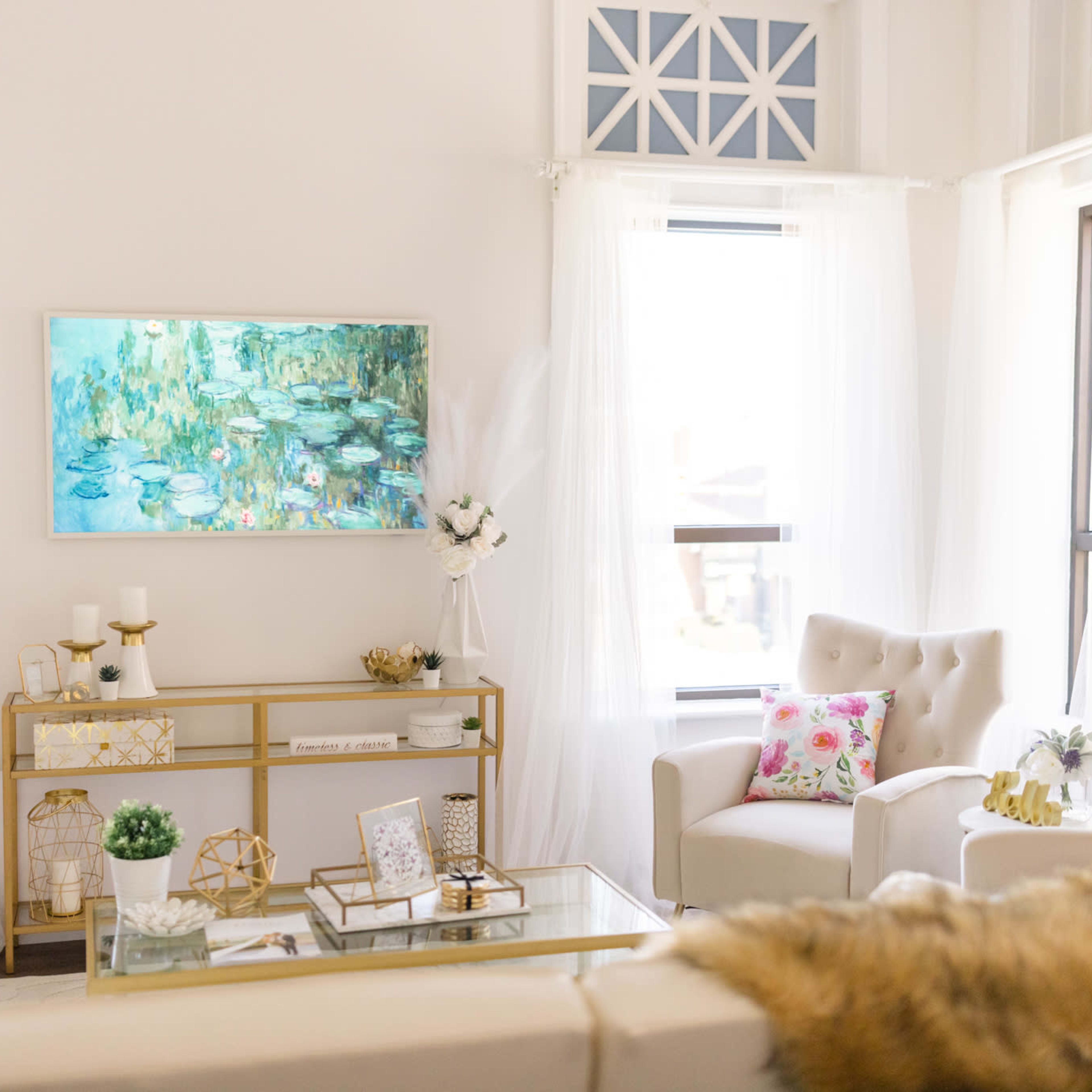A bright, modern living room with light-colored furniture, a colorful painting on the wall, and decorative elements like plants and pillows.