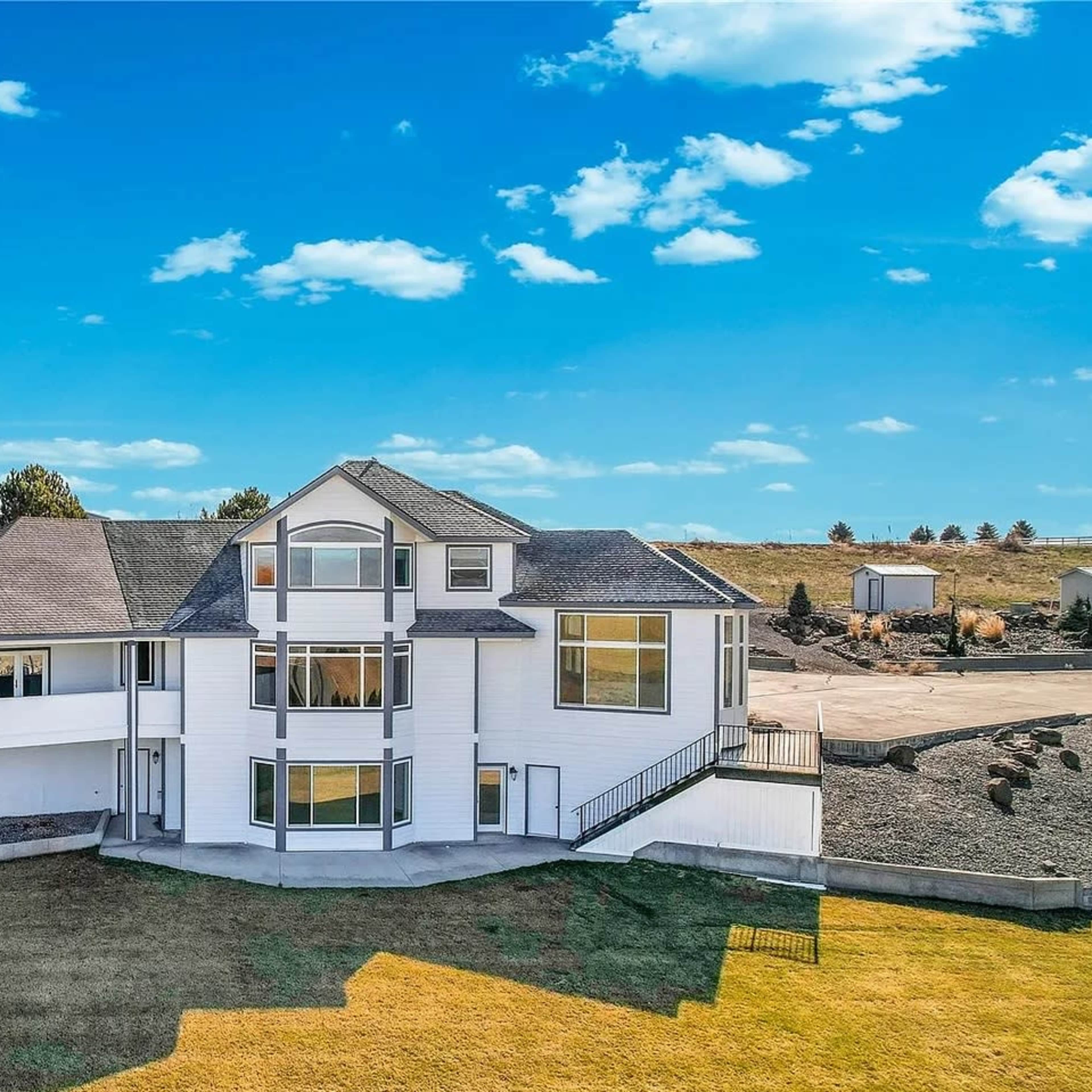 A modern two-story house with large windows and a landscaped yard is situated on a hillside.
