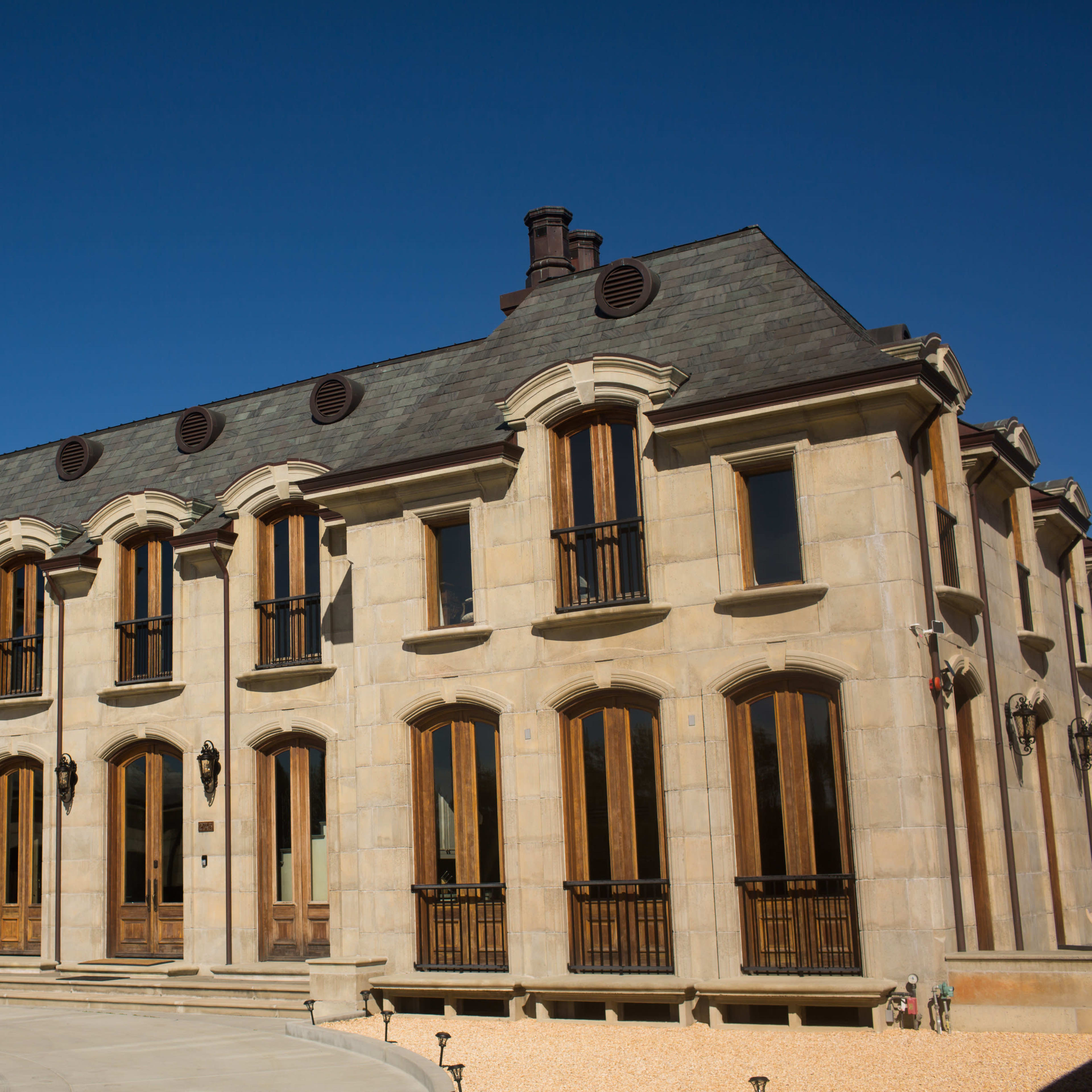 A large, multi-story stone mansion with arched windows and a sloped roof under a clear blue sky.