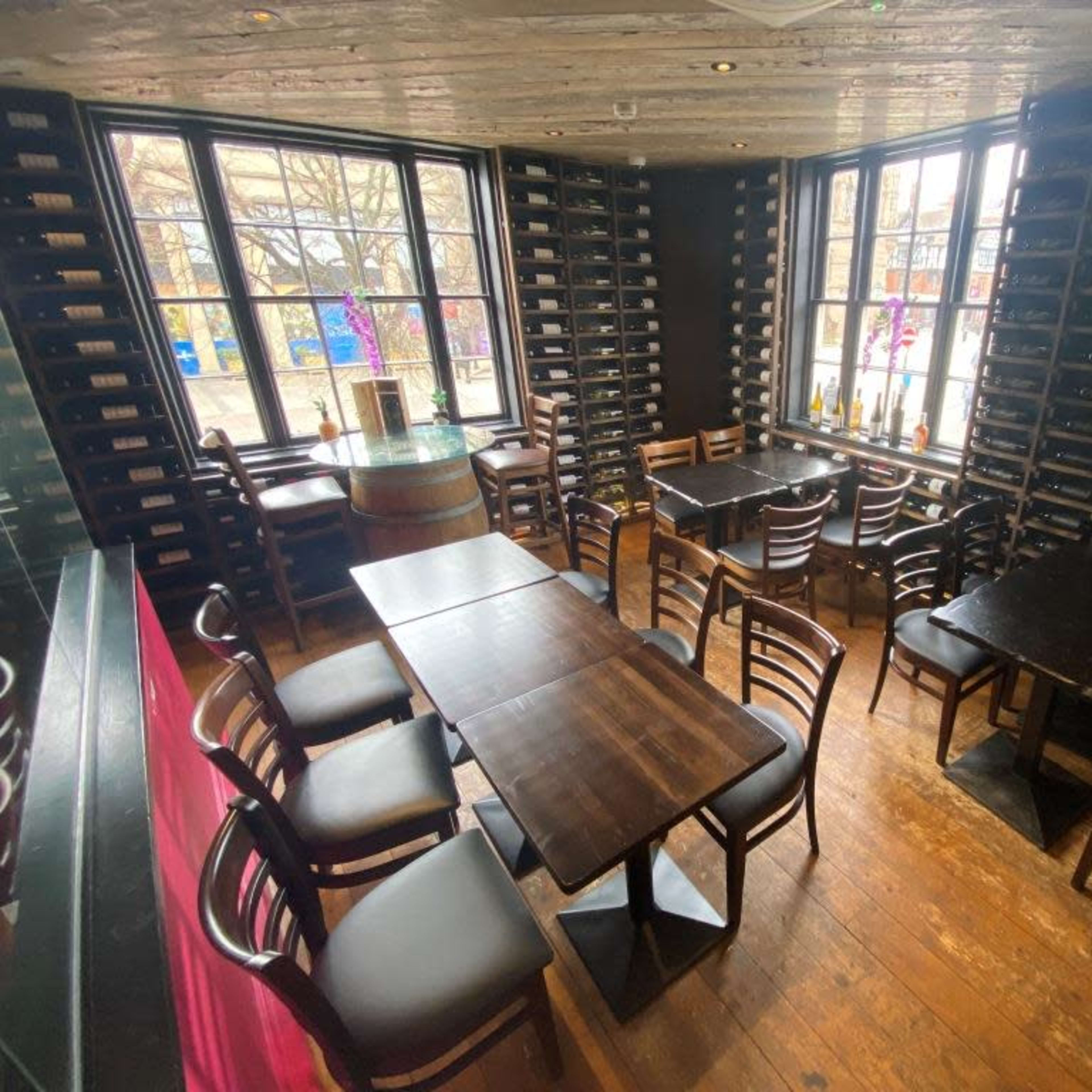 A dining area with several wooden tables and chairs, surrounded by wine racks filling the walls.