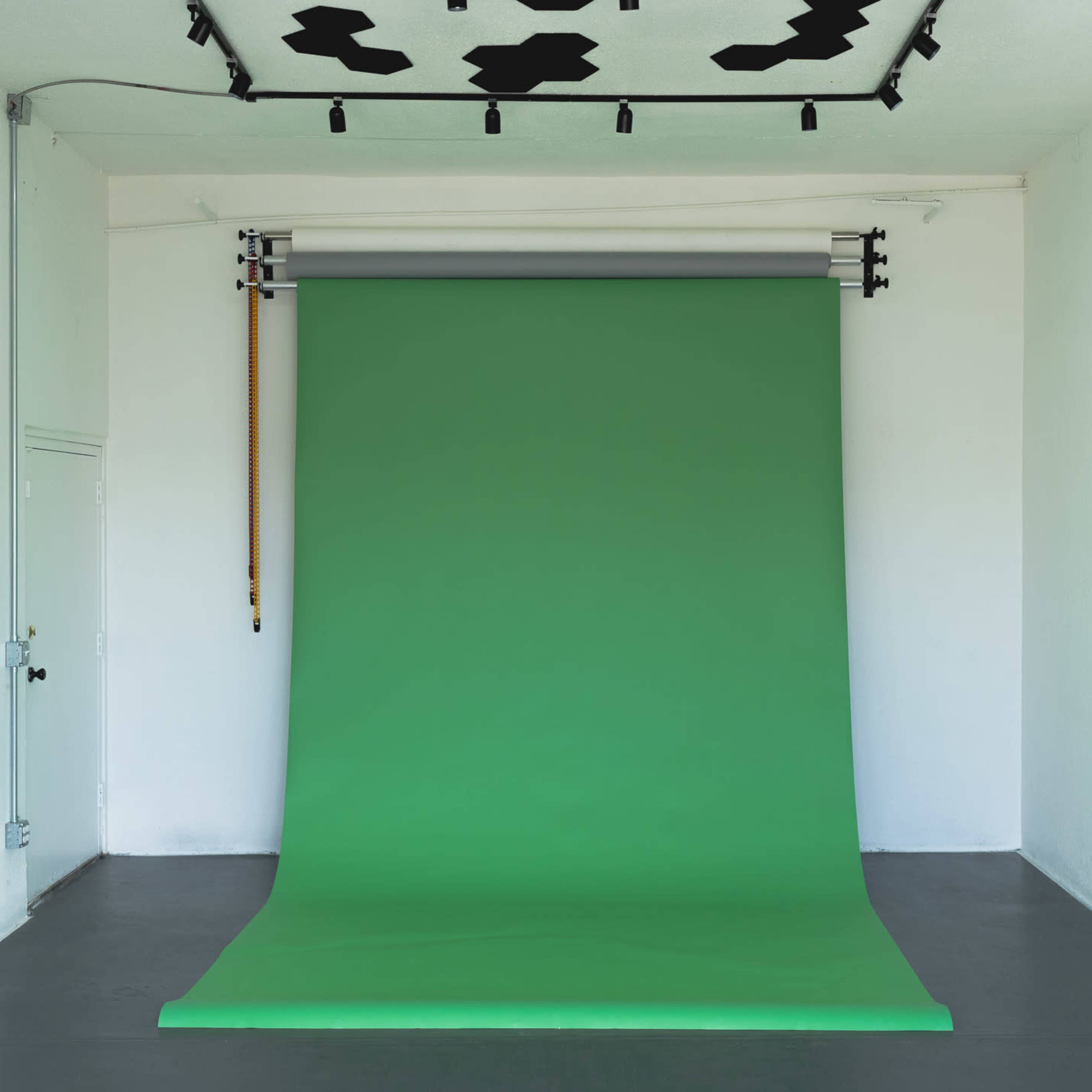 A studio space with a large green backdrop set up against a white wall.