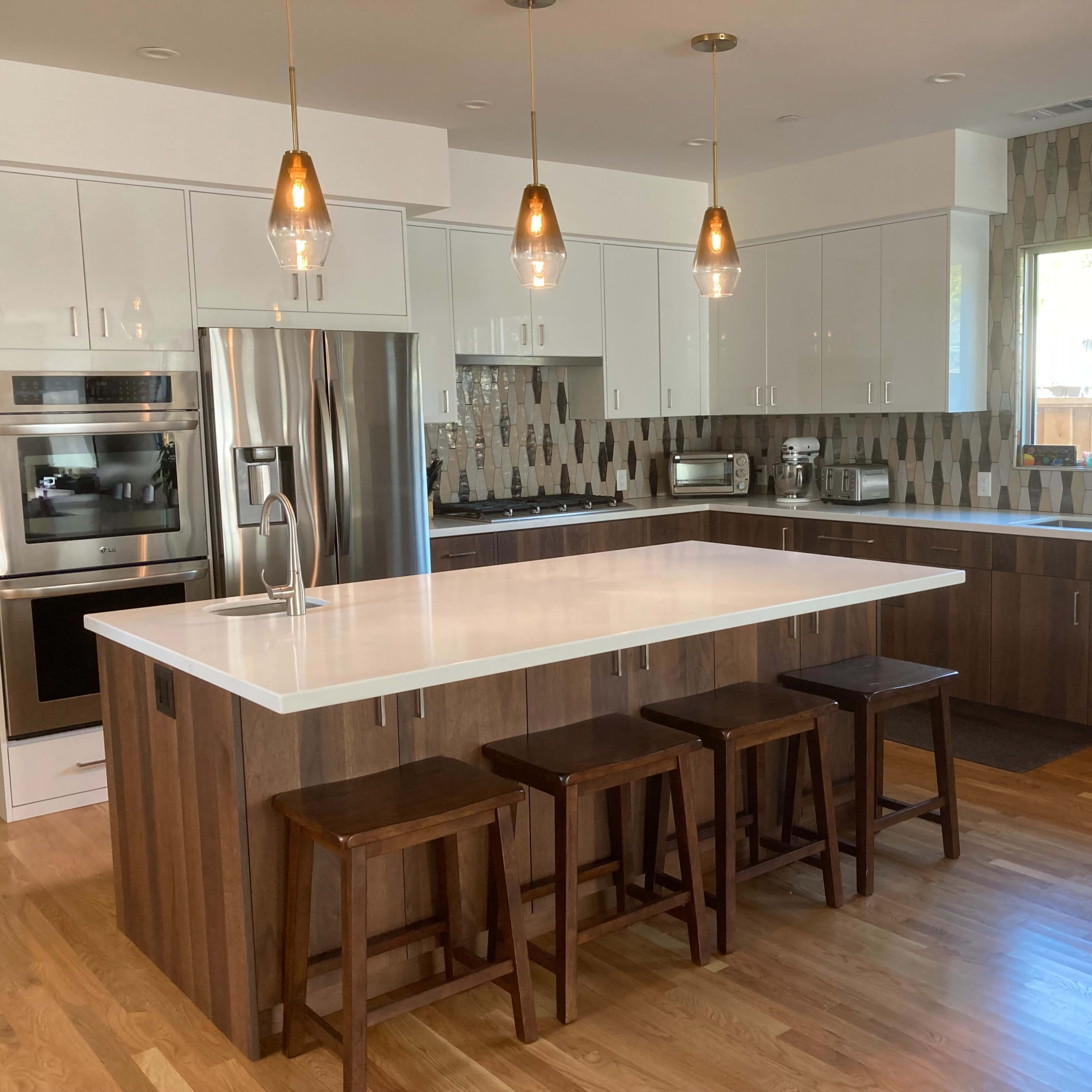 A modern kitchen with a large island, wooden bar stools, stainless steel appliances, and pendant lighting.