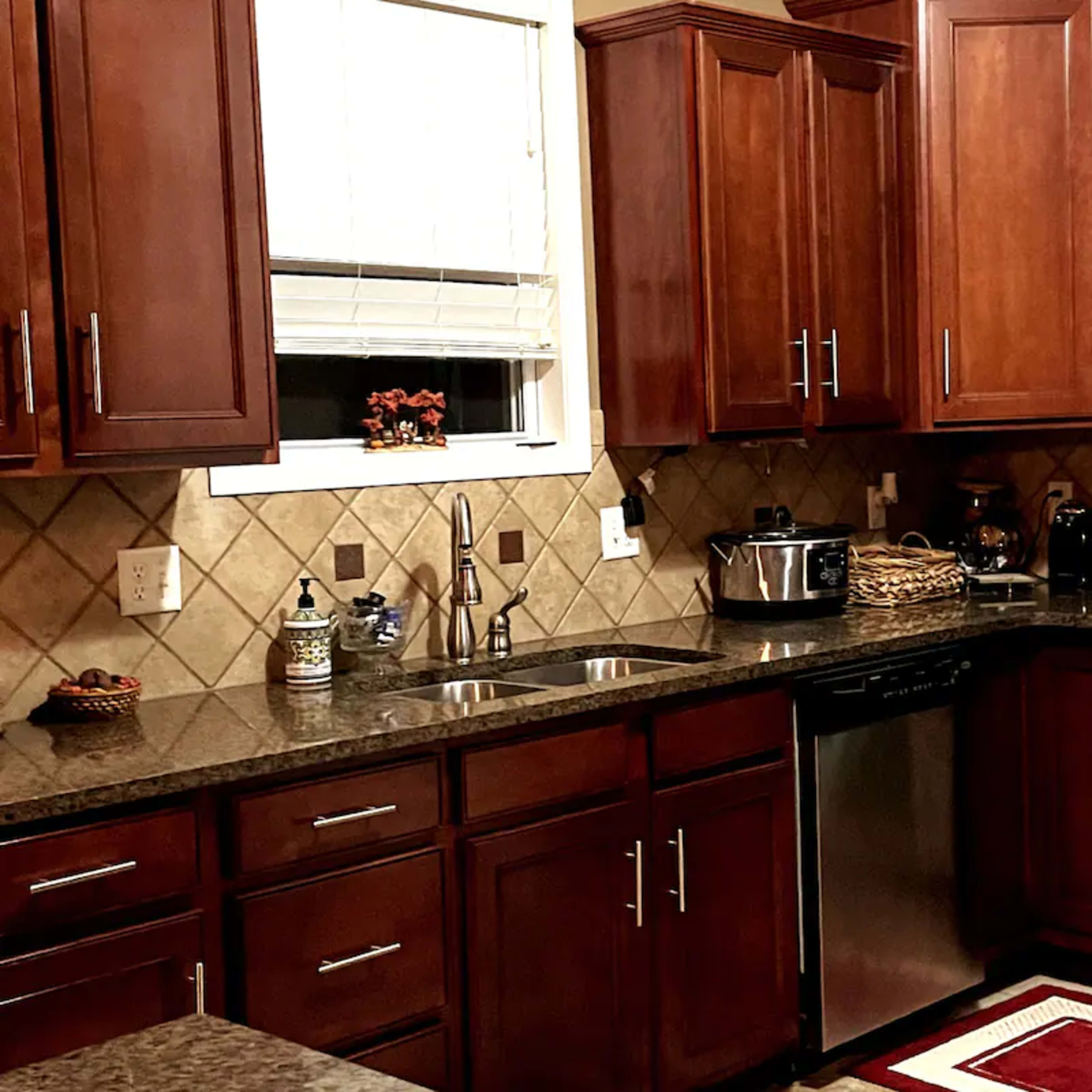 A kitchen with dark wood cabinetry, stainless steel appliances, and a tiled backsplash, featuring a double sink and a countertop.
