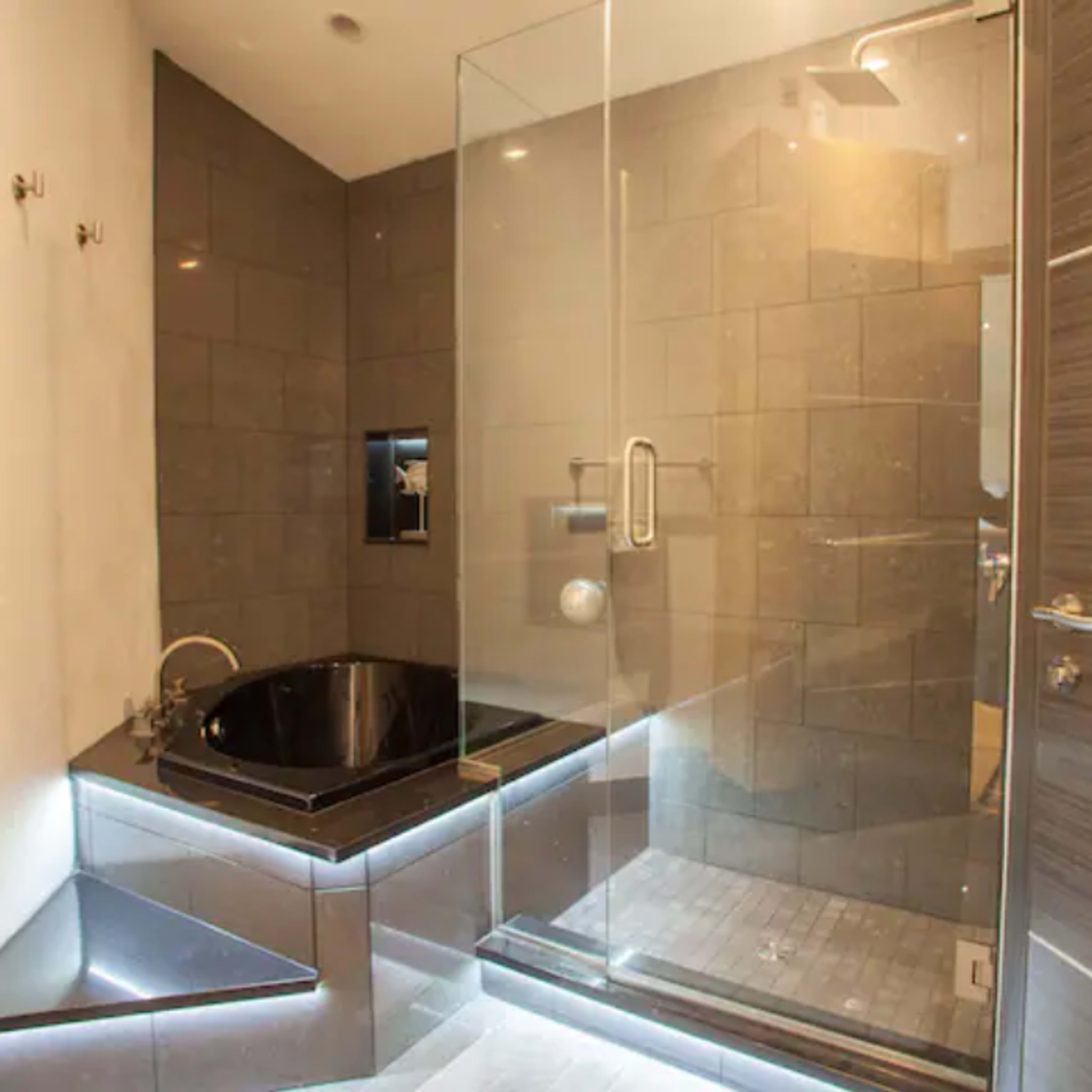A modern bathroom featuring a shower enclosure, a black tub, and gray tiled walls.
