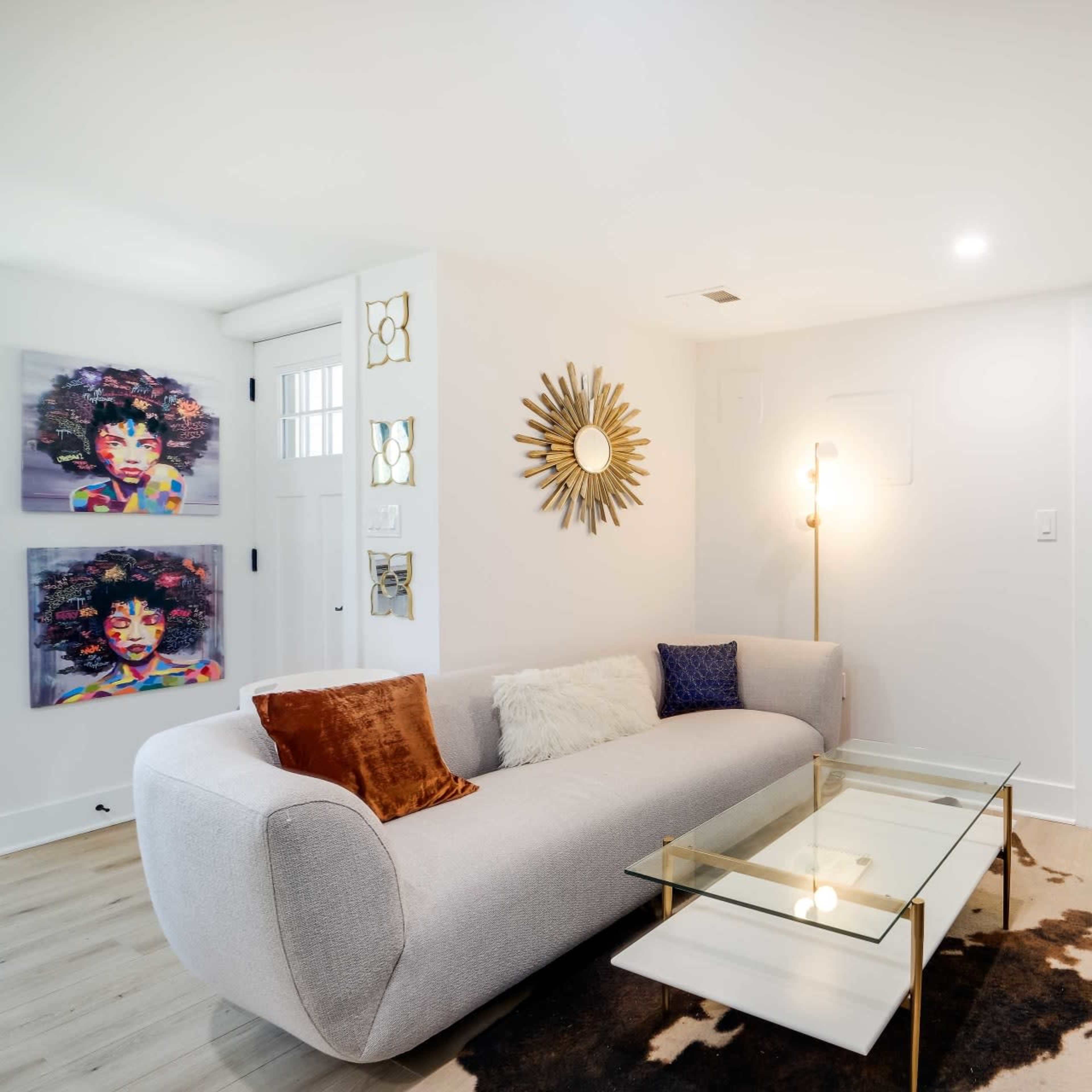A modern living room with a curved gray sofa, a glass coffee table, and decorative artworks on the walls, including colorful portraits.
