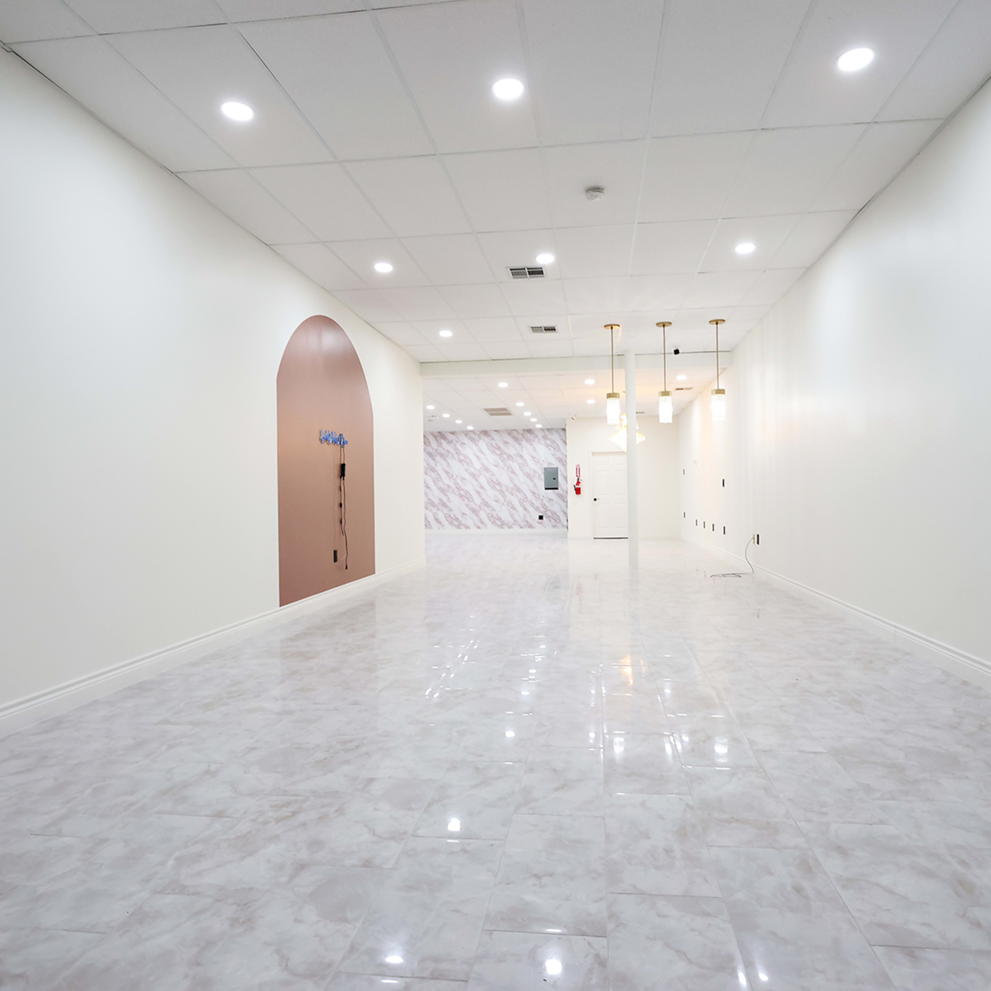 A spacious, well-lit hallway with white walls and shiny marble flooring, featuring decorative elements at one end.
