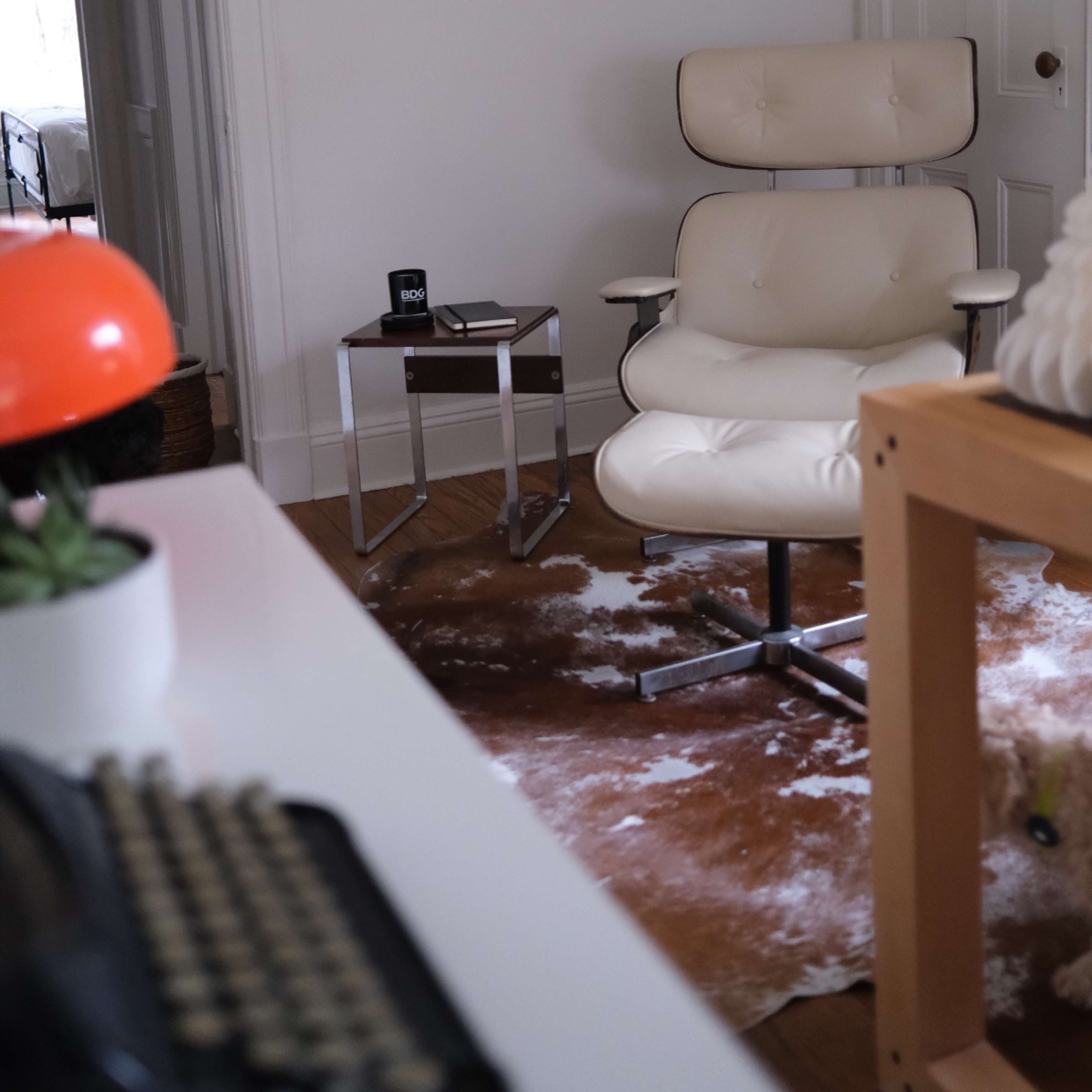 A white leather chair sits next to a glass side table in a bright room with wooden flooring and a cowhide rug.