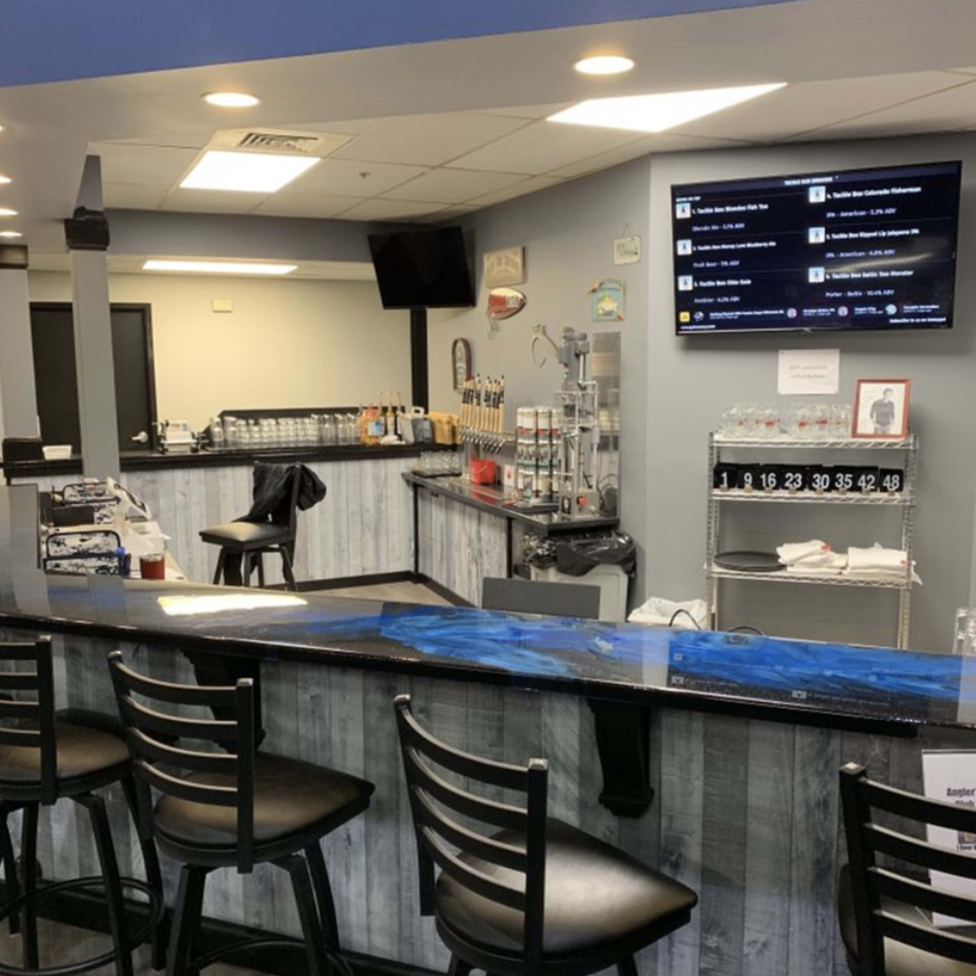 A modern bar area features a long counter with black stools, a variety of beer taps, and a television mounted on the wall.