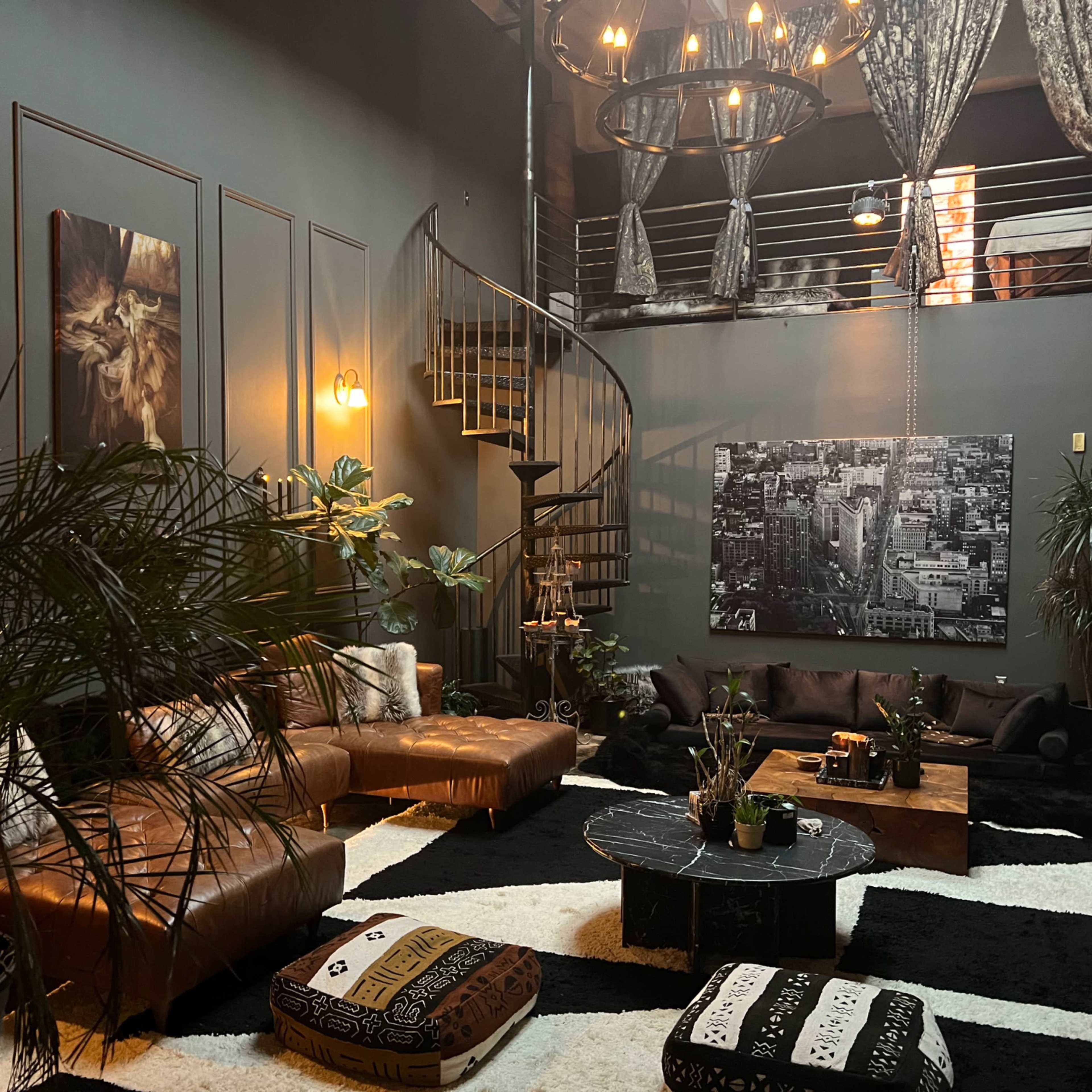 A stylish, modern living room with leather sofas, a circular staircase, and large plants, featuring dark walls and contrasting furniture.