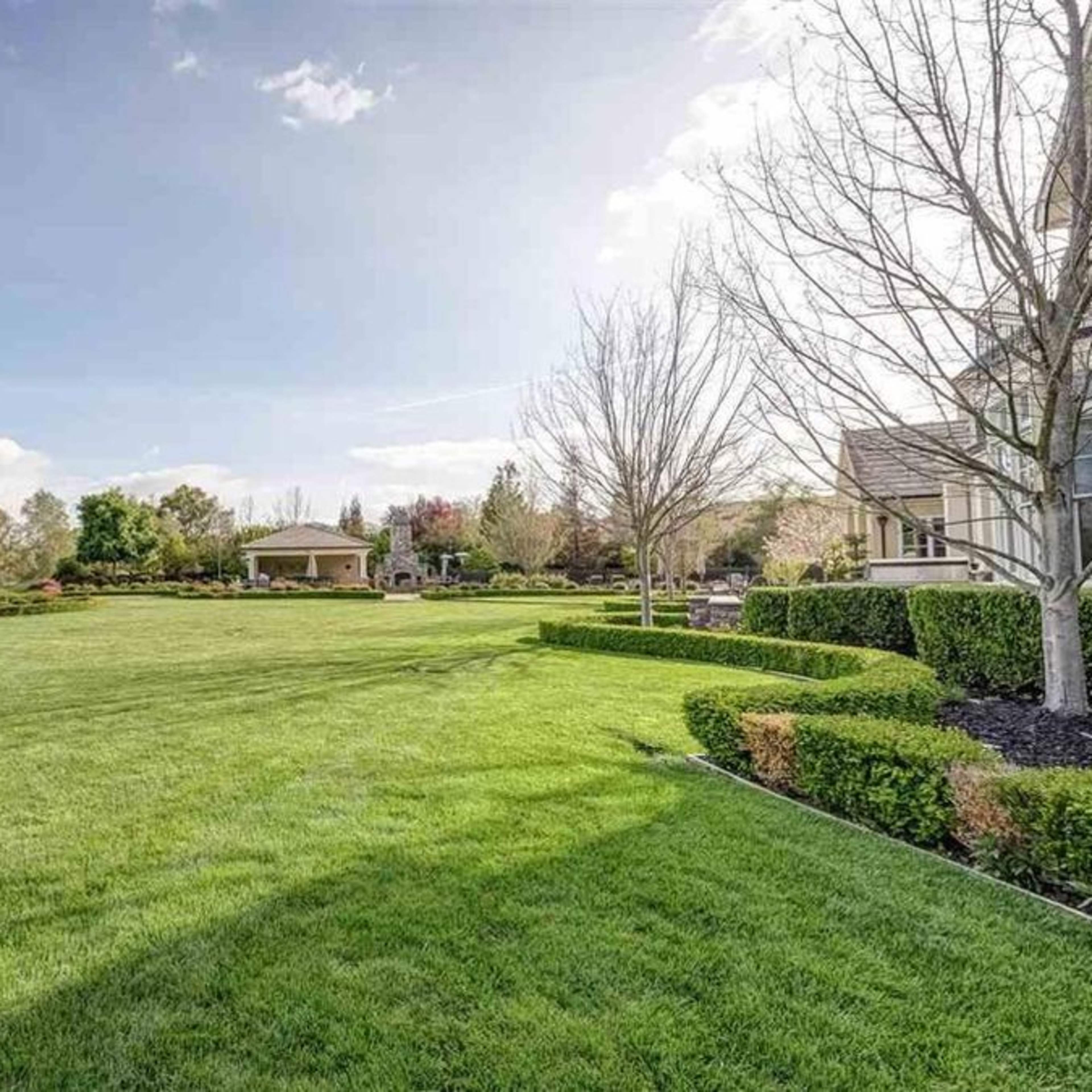 A spacious, well-maintained lawn surrounded by trees and a gazebo in a residential area.