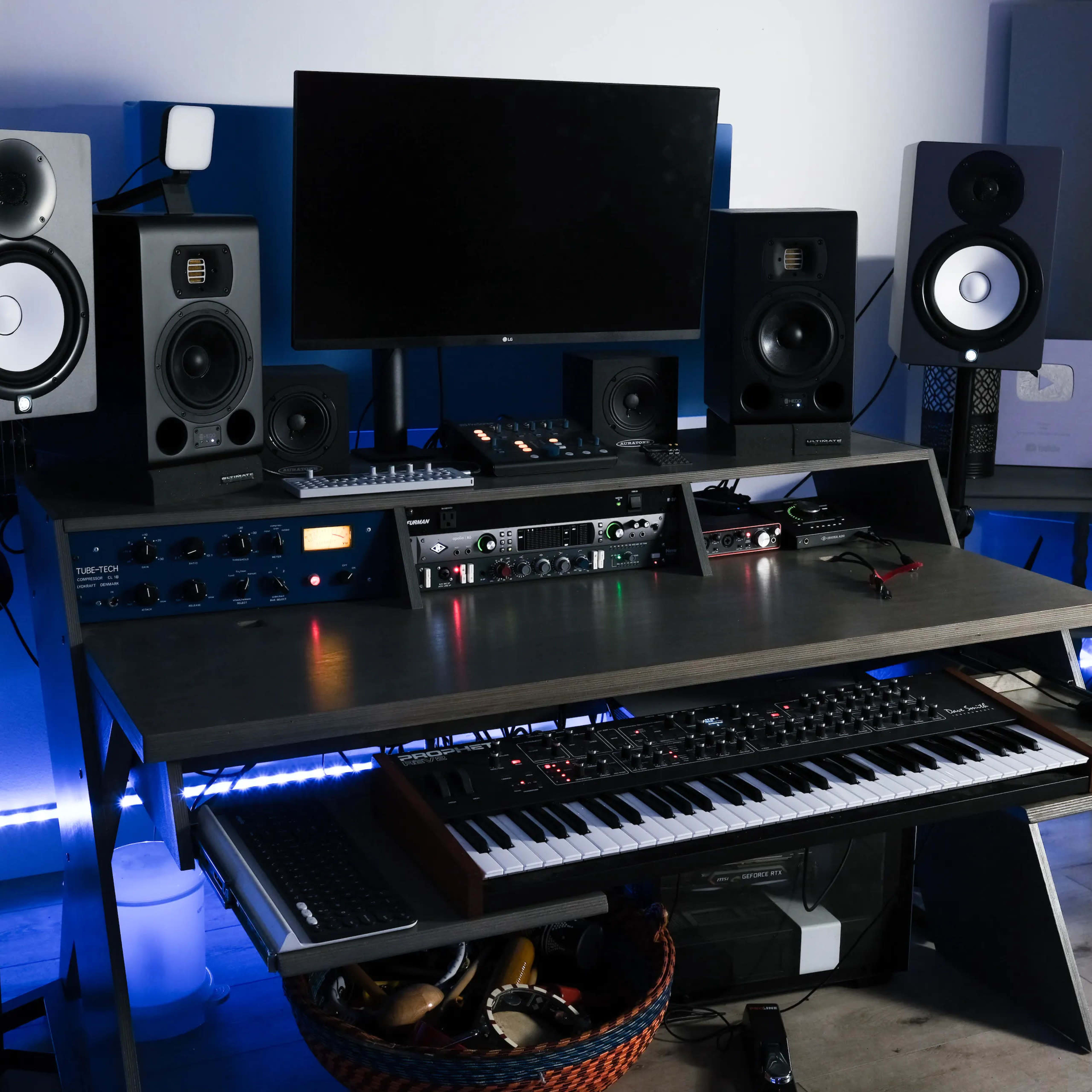 A music production setup featuring a desk with a keyboard, audio monitors, a computer screen, and various audio equipment.