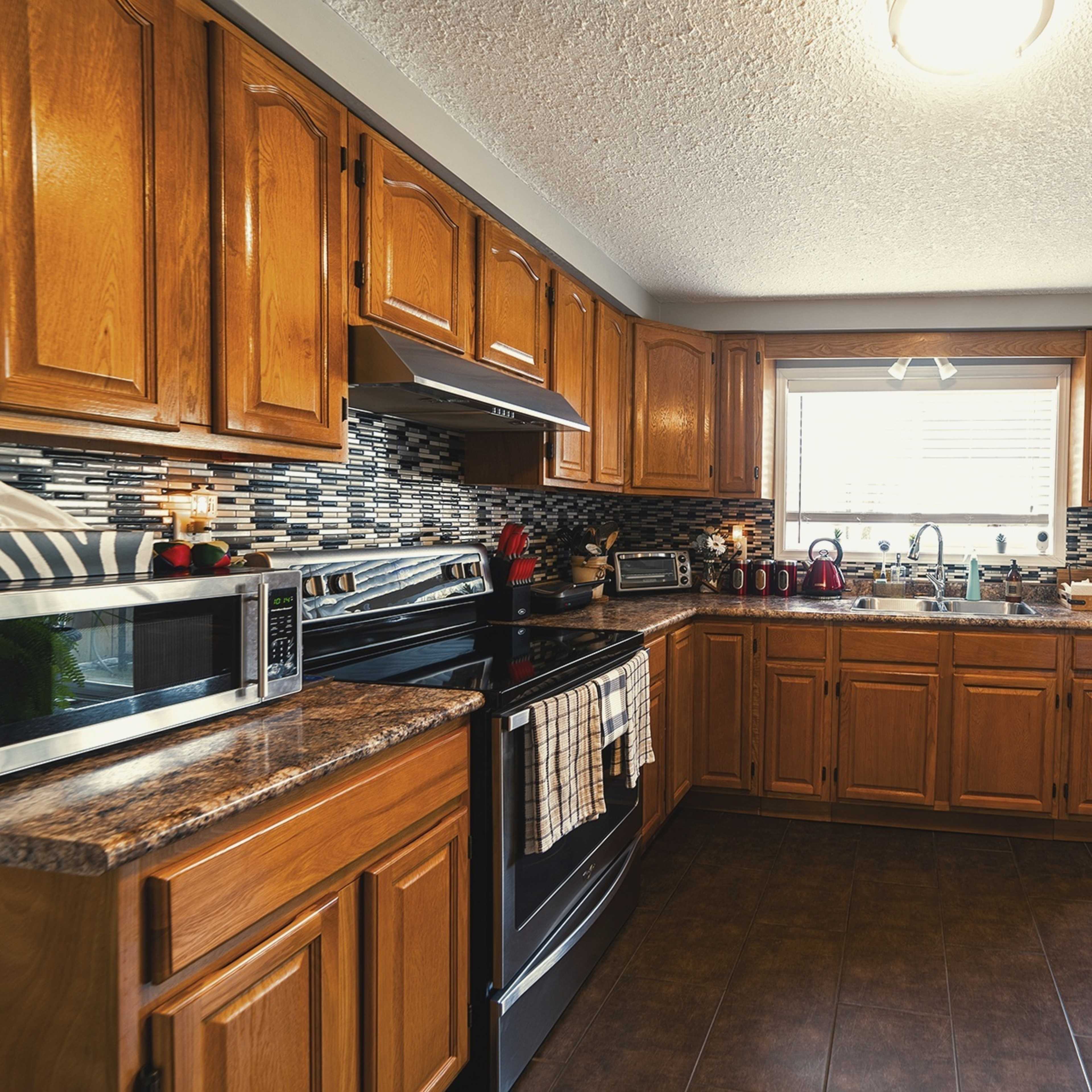 A modern kitchen features wooden cabinets, stainless steel appliances, and a window overlooking an outdoor area.