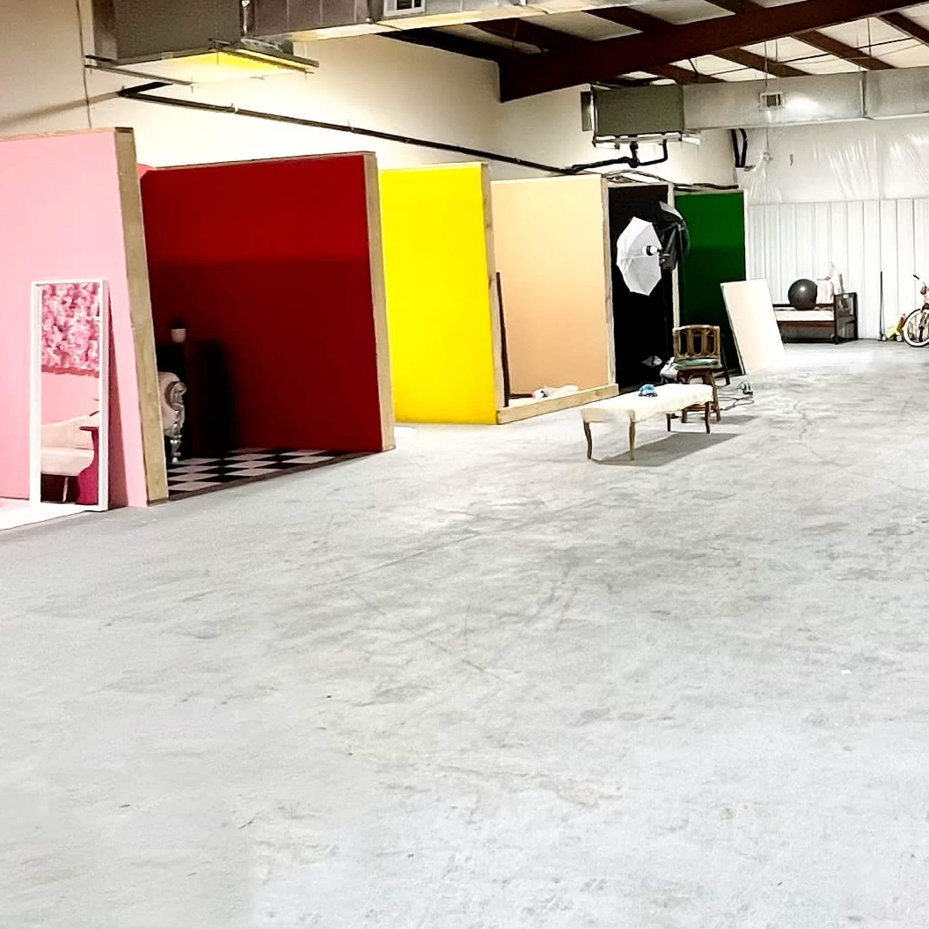 A spacious garage or studio area with vibrant colored backdrops, two parked sports cars, and minimal furniture.