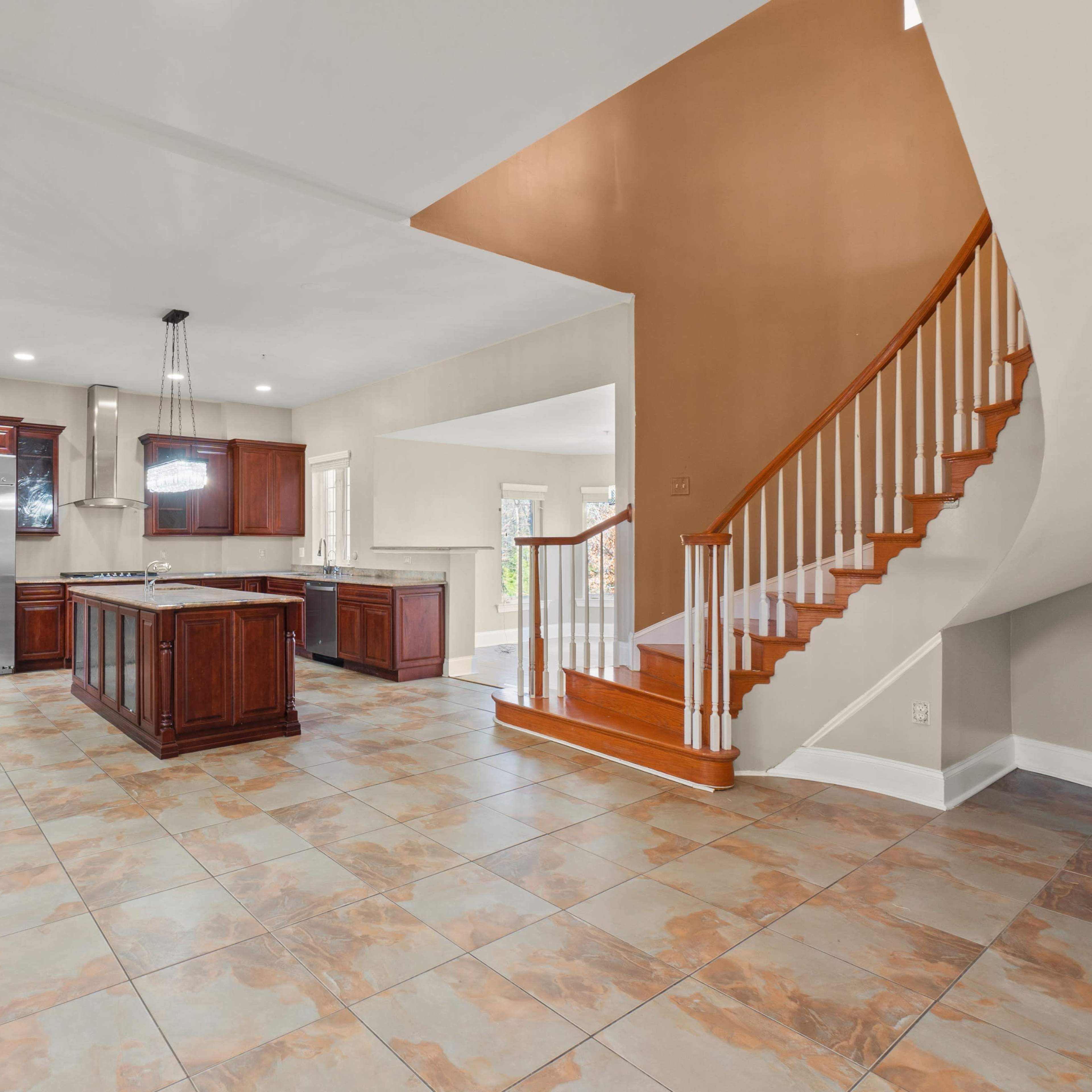 A modern kitchen with dark wood cabinets and a large island, leading to a staircase with wooden railings in a spacious open area.