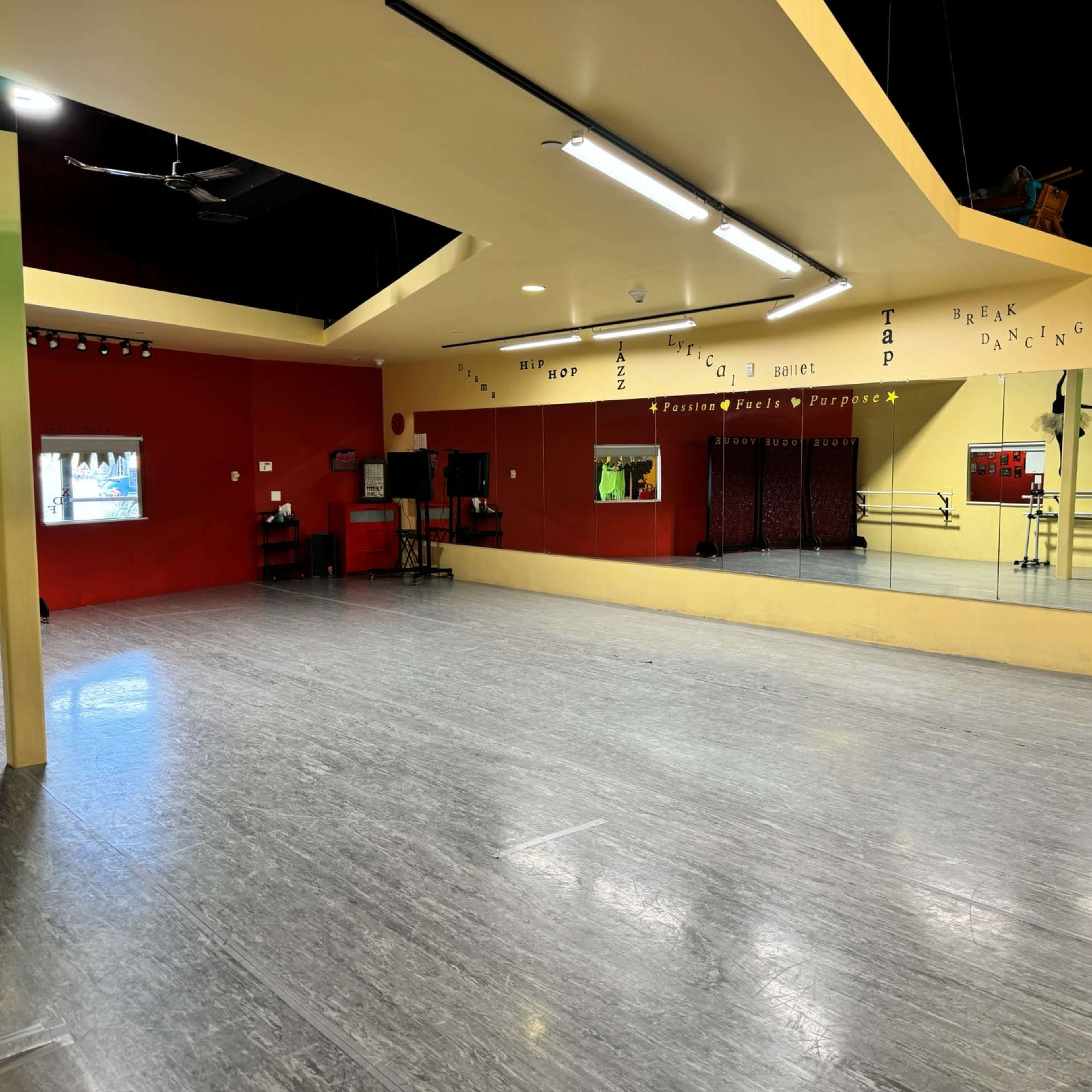 A spacious dance studio with wooden flooring, mirrors along one wall, and colorful painted accents.