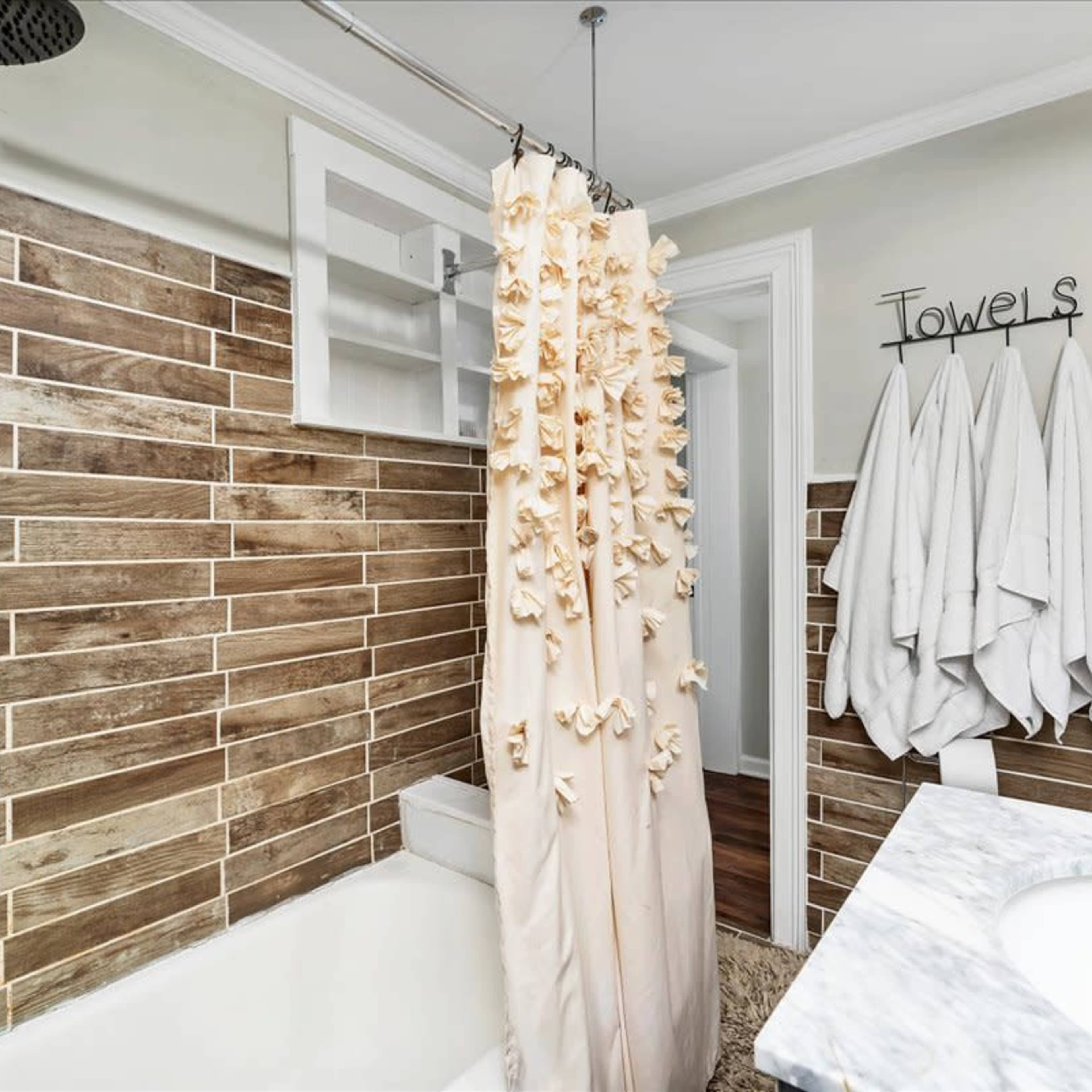 A bathroom with a shower curtain, wooden tiled walls, hanging white towels, and a marble countertop.