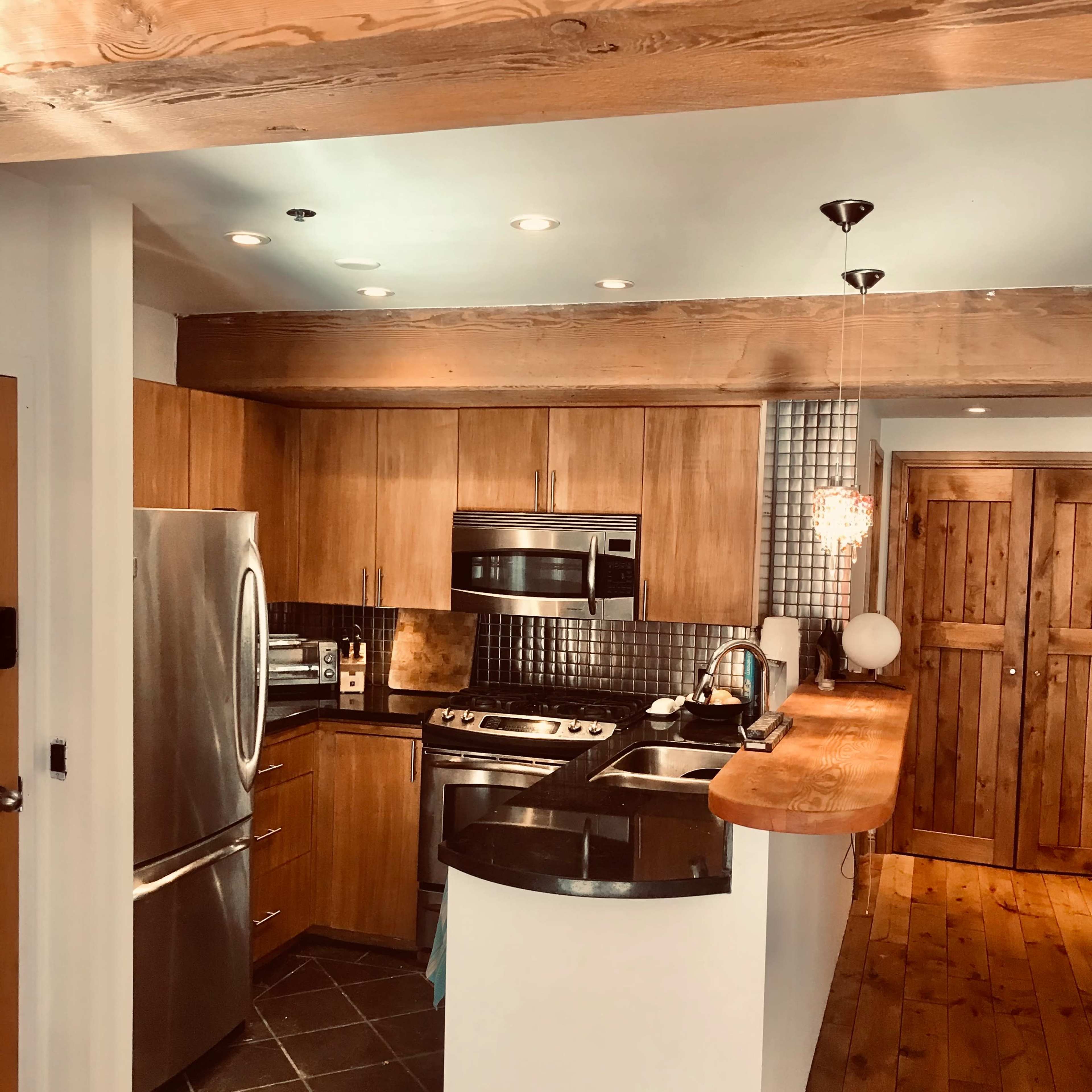 A modern kitchen features stainless steel appliances, wood cabinetry, and a long counter with a seating area.