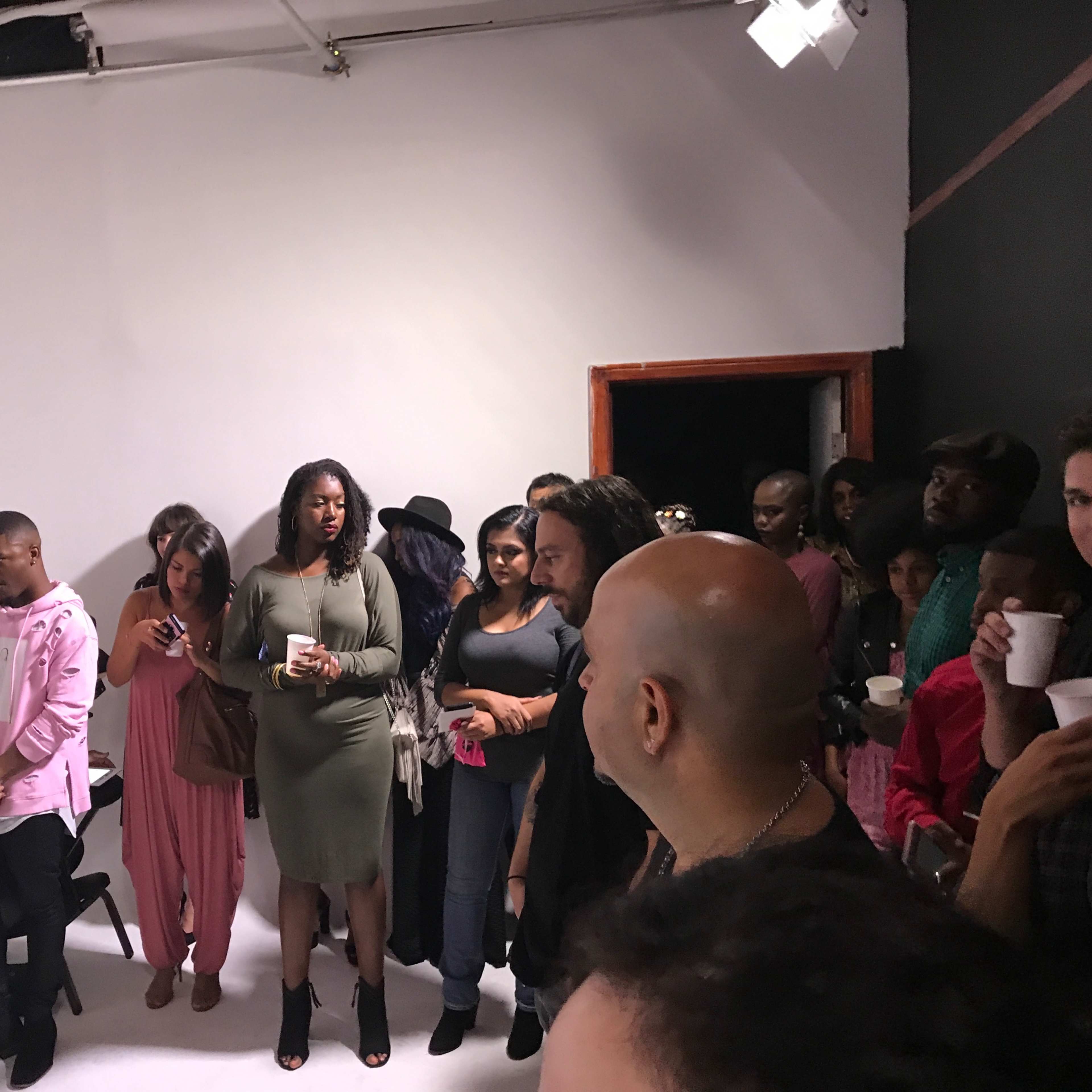 A group of people stands closely together in a studio space, attentively watching an event or presentation.