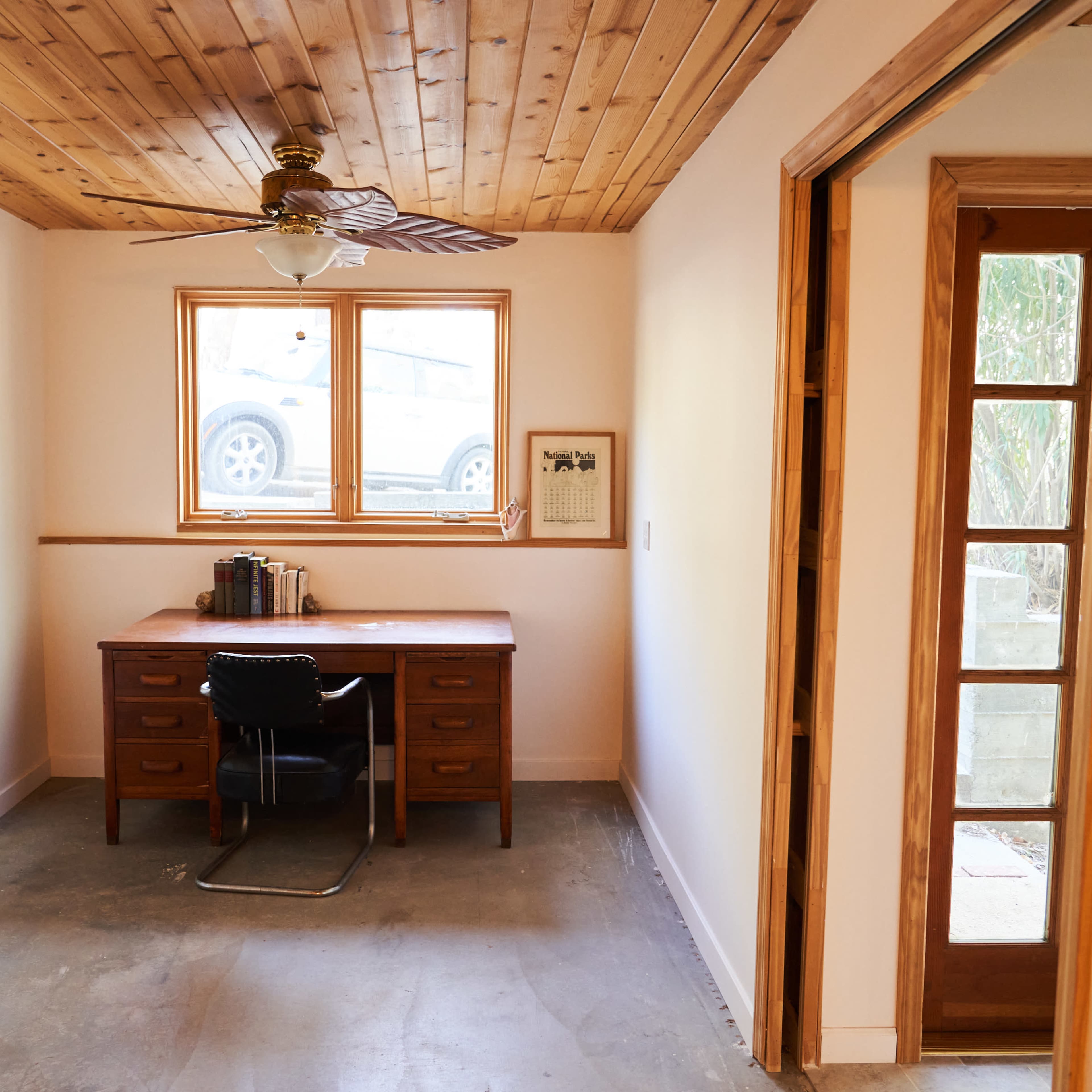 A partially finished room with a wooden ceiling, a desk with a chair, and a window facing an outdoor view.