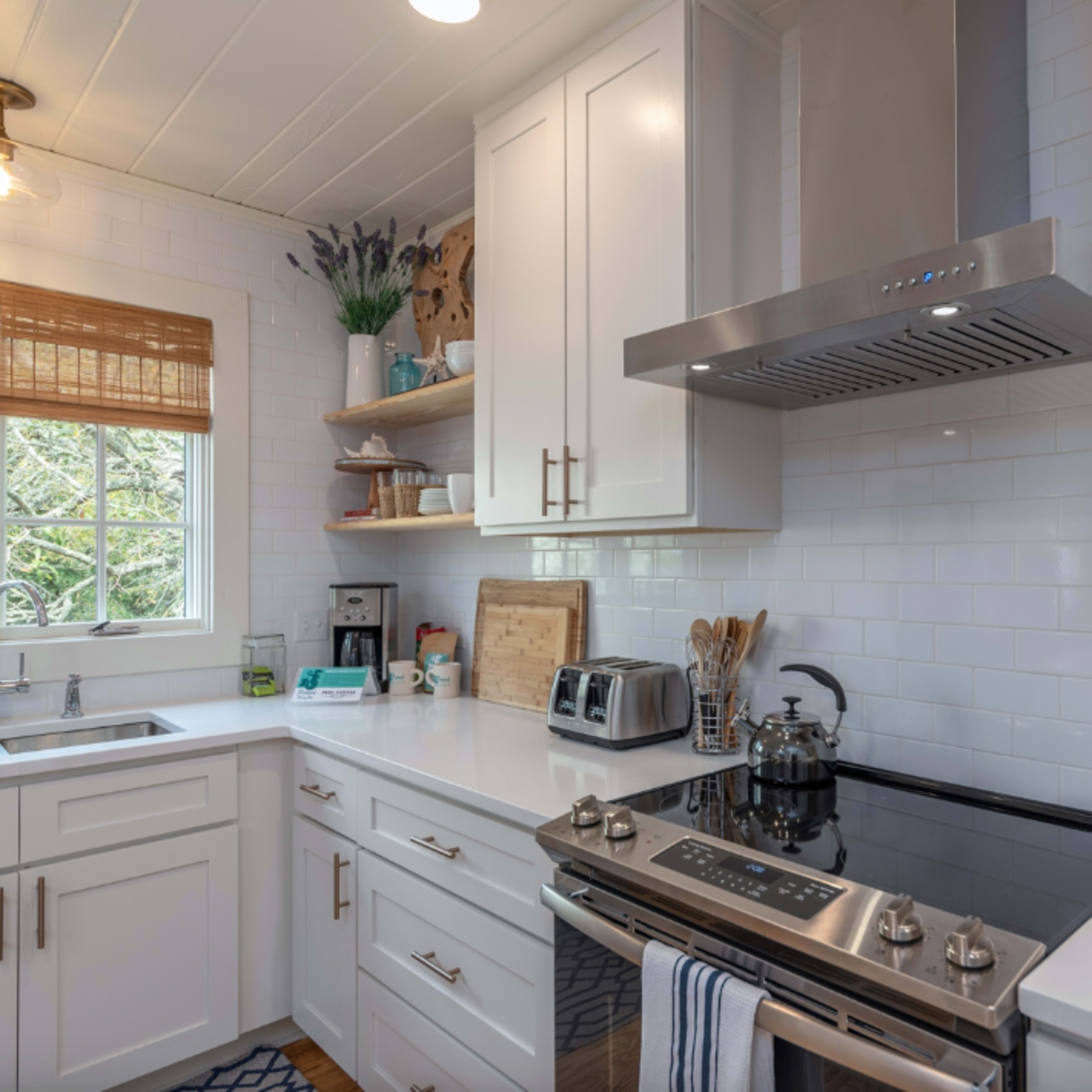 A modern kitchen features white cabinets, a stainless steel stove, and natural light streaming through a window.