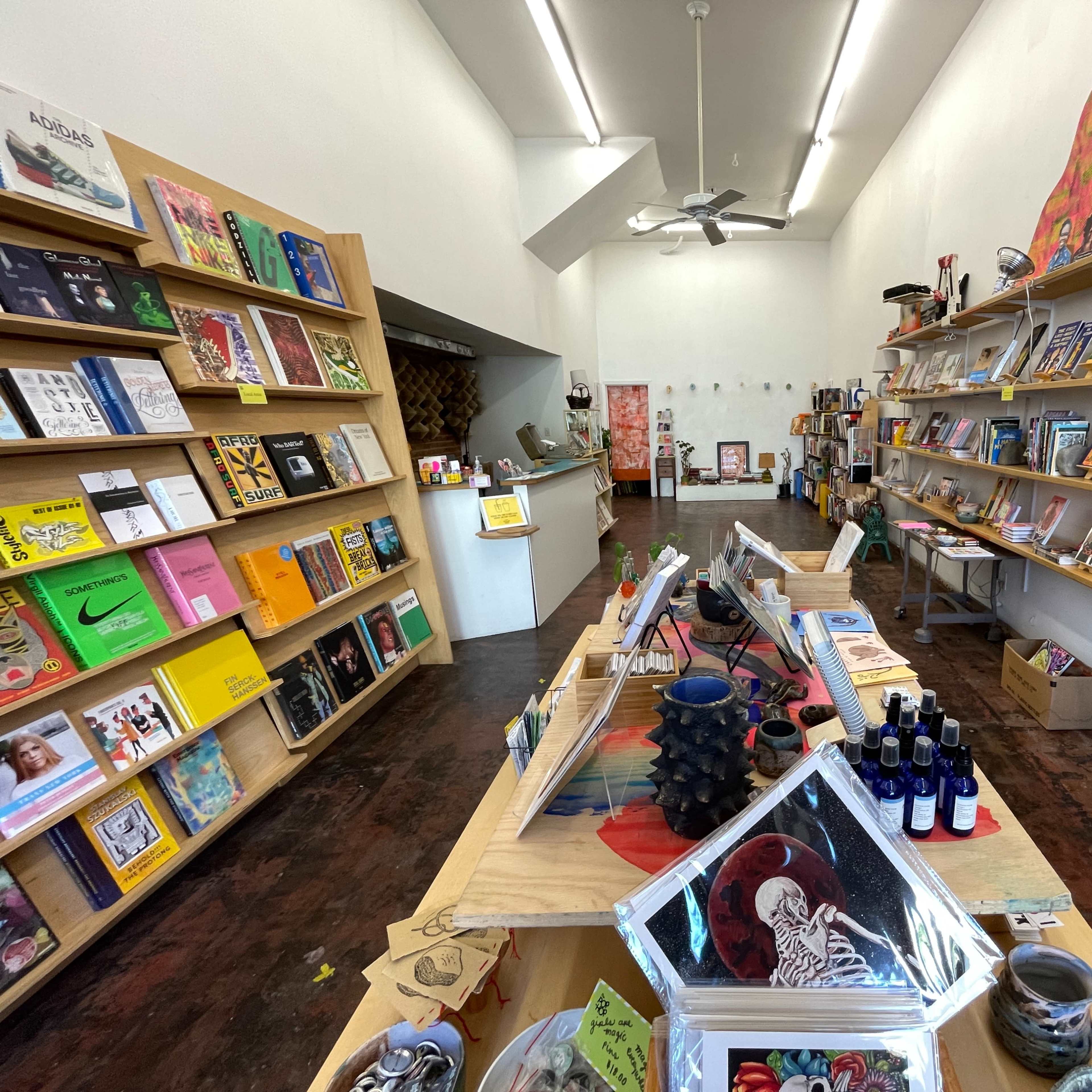 The interior of a bookstore with wooden shelves displaying various books and art products, and a checkout counter in the foreground.