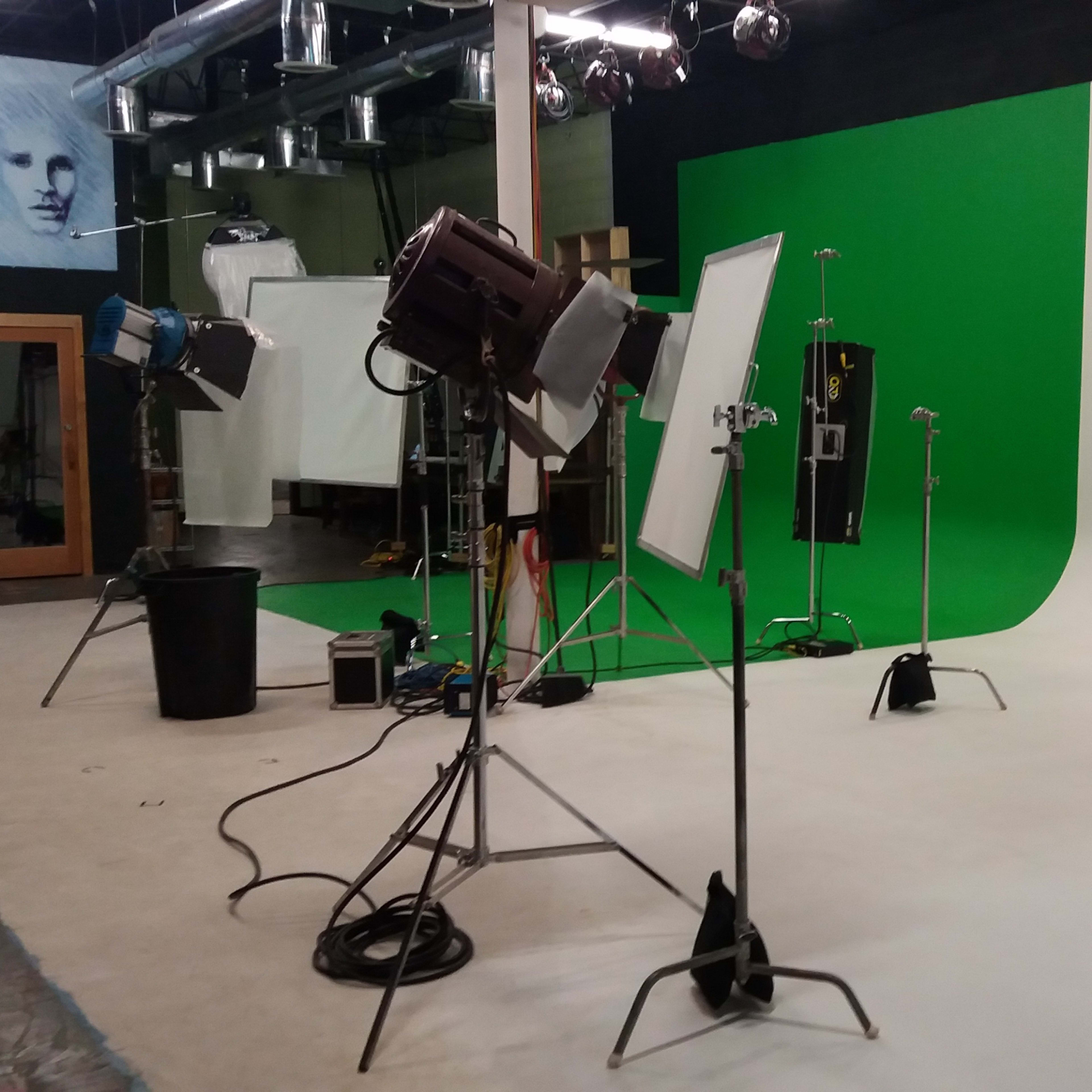 A photography studio equipped with lighting equipment, a green screen, and a white backdrop.