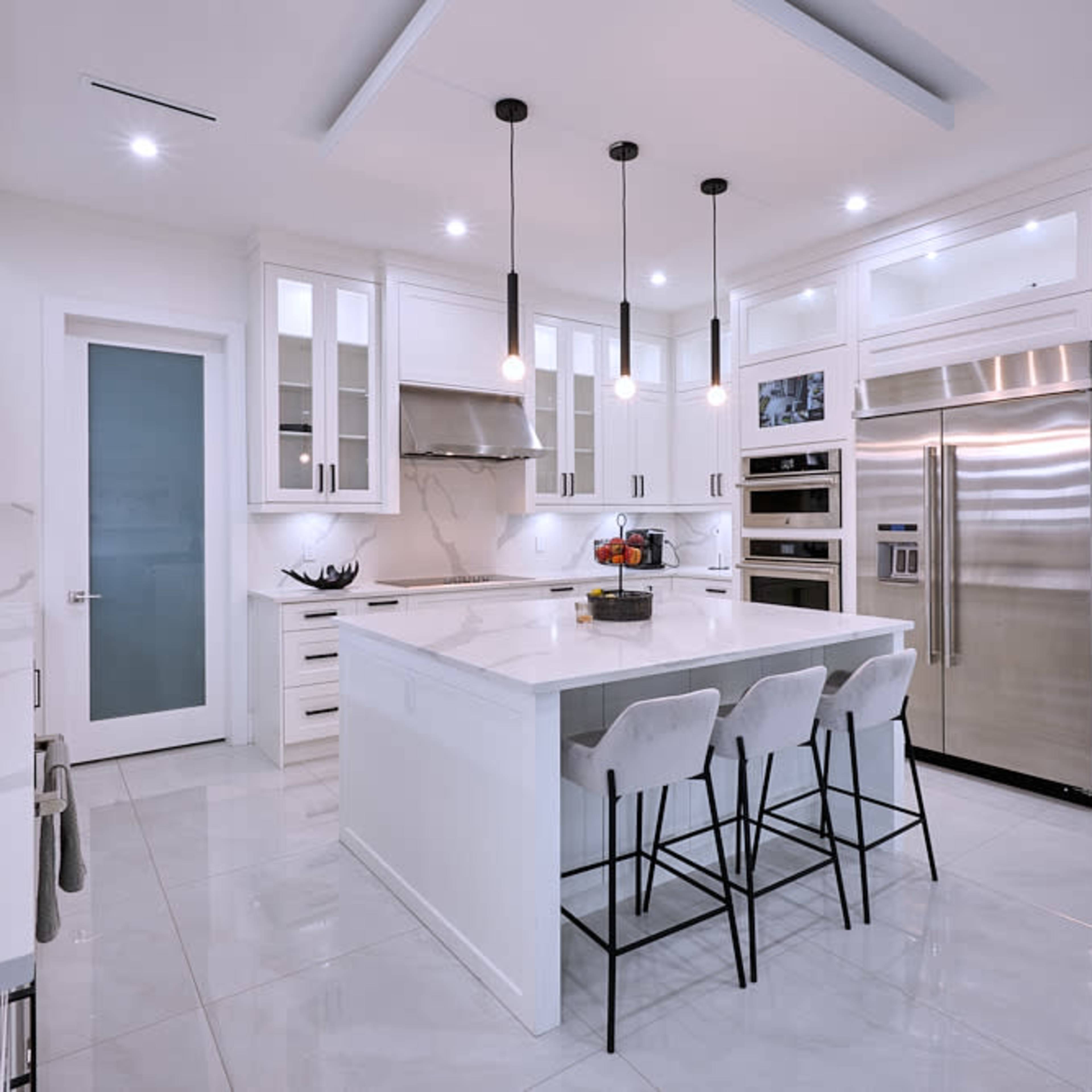 A modern kitchen features white cabinets, a large central island with seating, and stainless steel appliances.