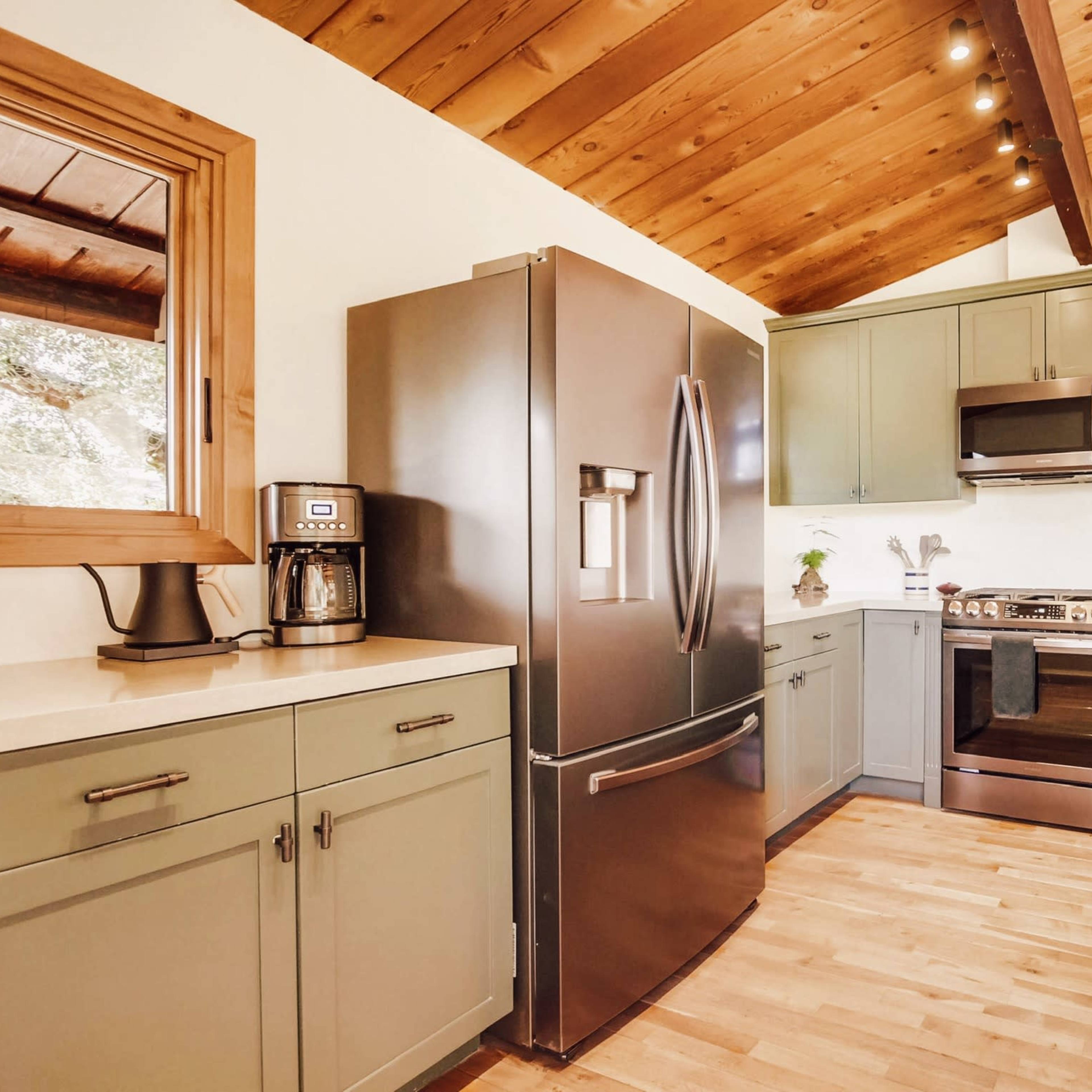 A modern kitchen features gray cabinetry, stainless steel appliances, and wooden beam ceilings.
