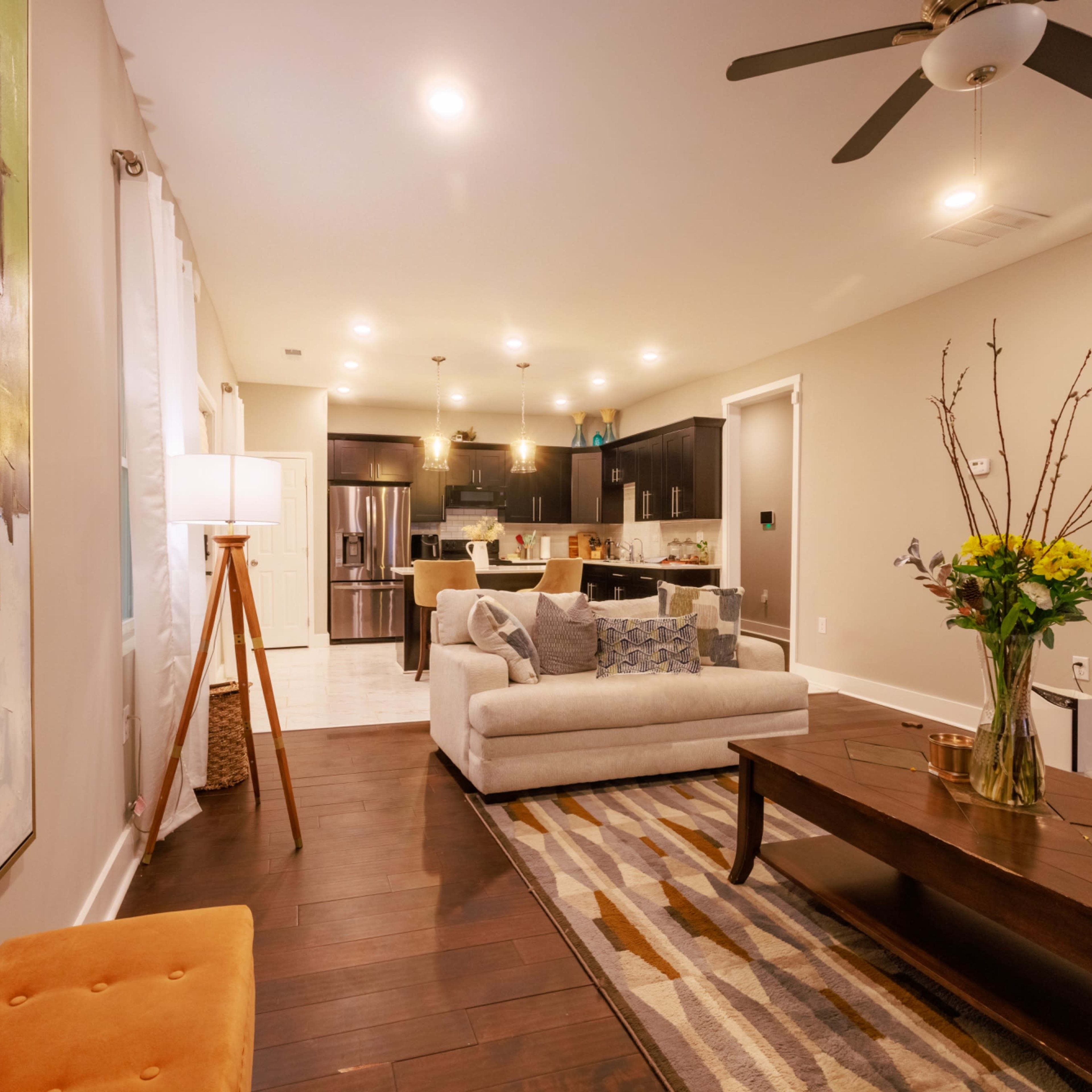 A modern living room with a gray sofa, a coffee table, a decorative floor lamp, and a kitchen visible in the background.