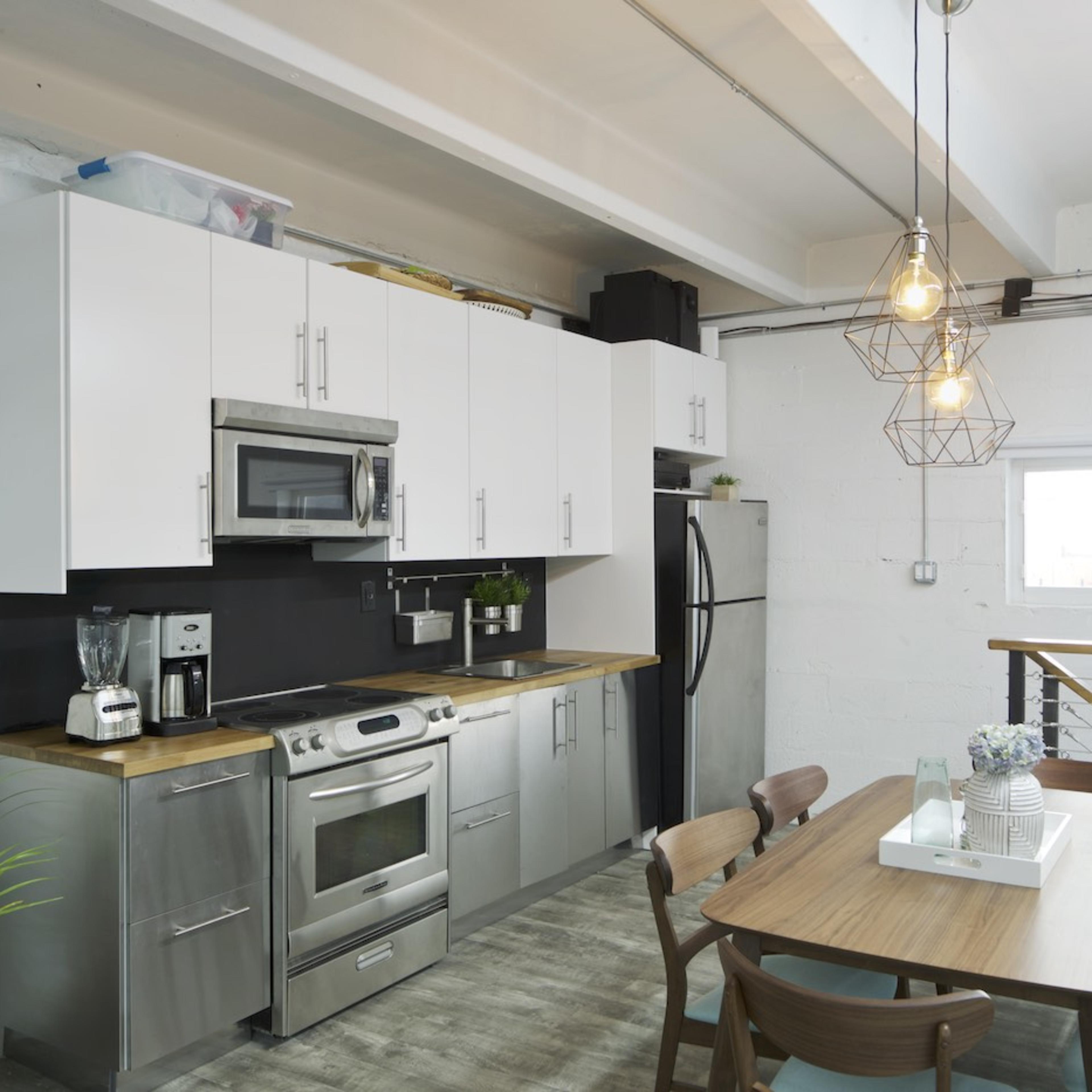 A modern kitchen with stainless steel appliances, white cabinets, and a wooden dining table.