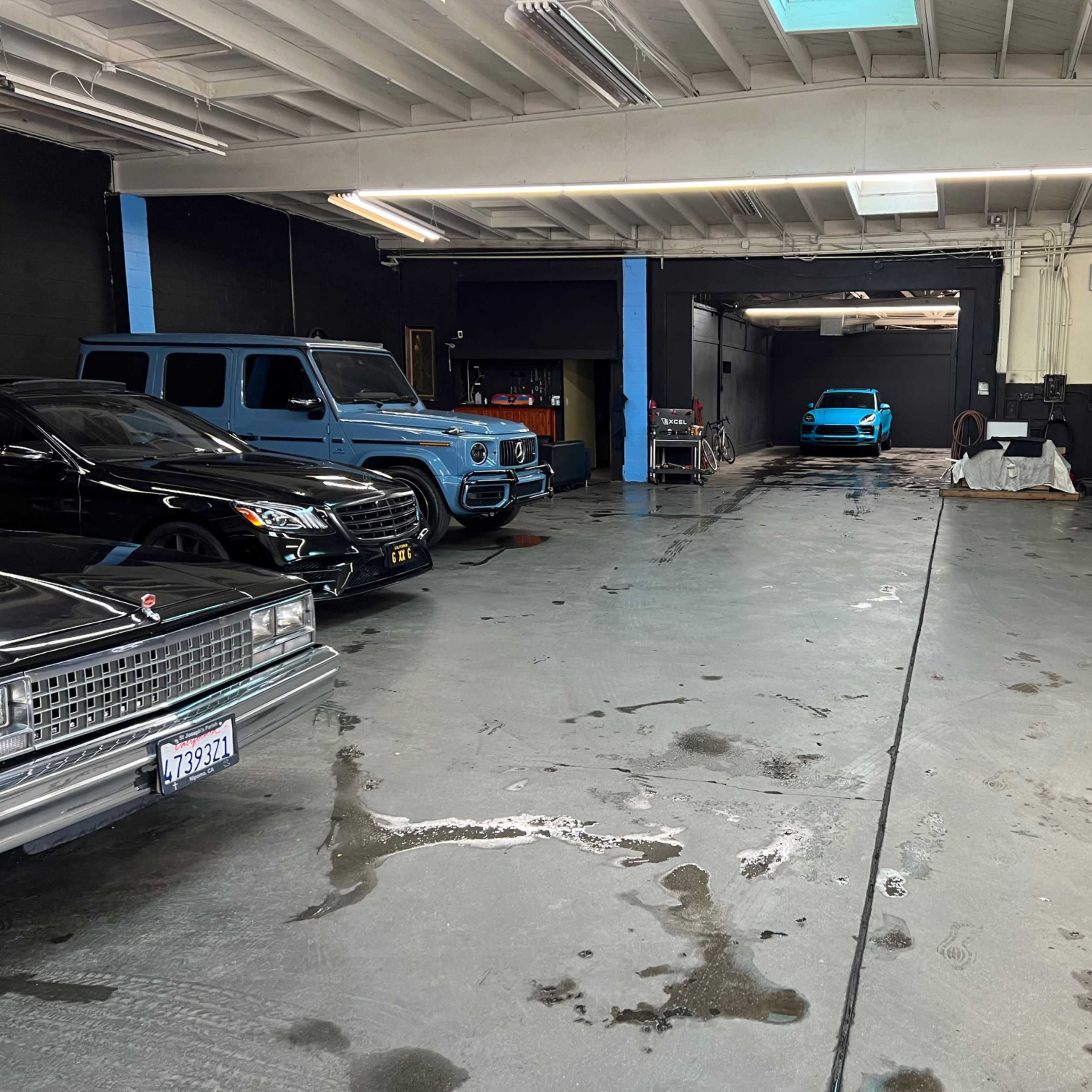 A spacious garage with several luxury vehicles, including a black SUV, a vintage car, and a blue sports car, arranged in an orderly manner.