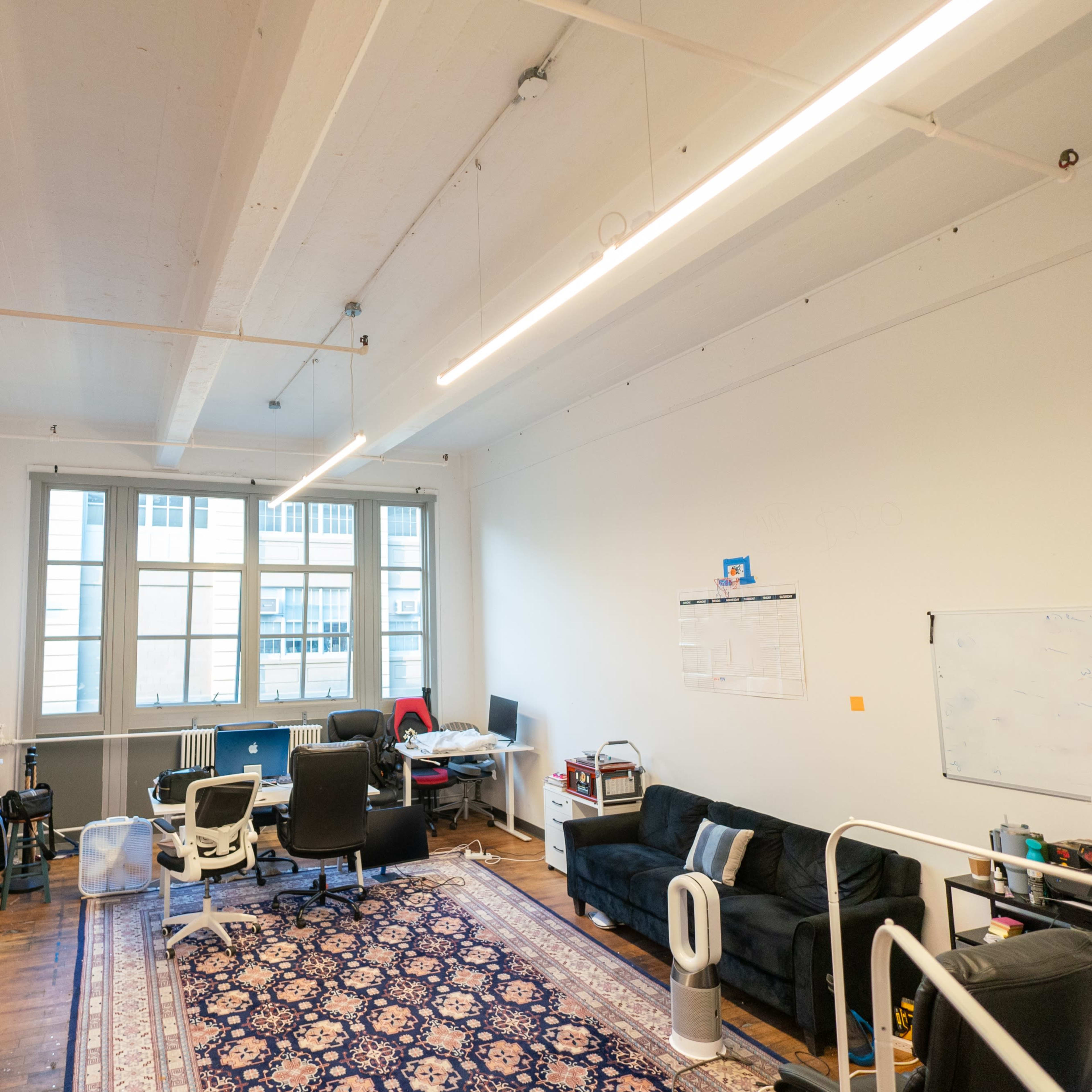 A spacious office with a sofa, desks, and colorful rolls of material hanging on the wall.