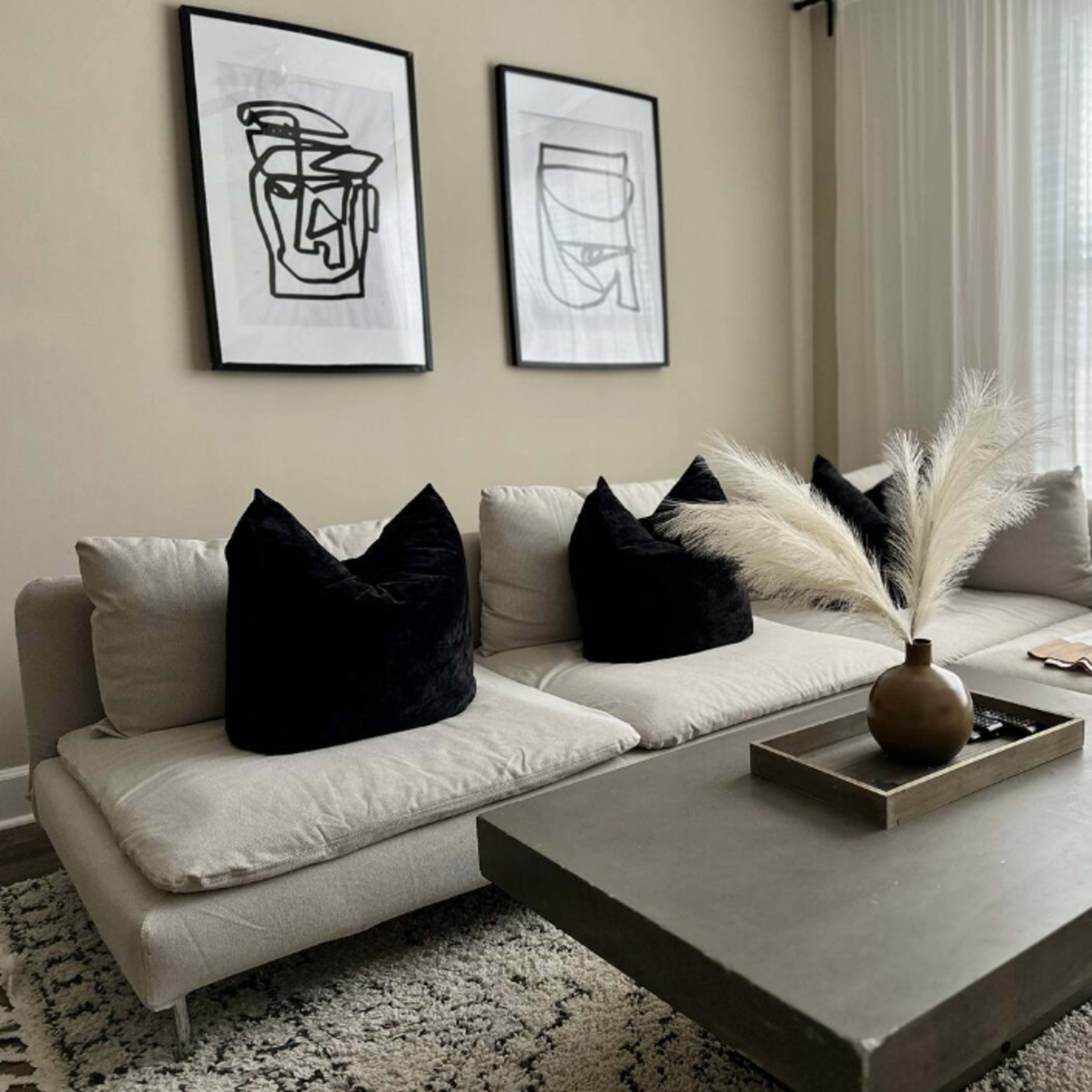 A modern living room features a sectional sofa with black pillows, a concrete coffee table, and framed abstract art on the walls.