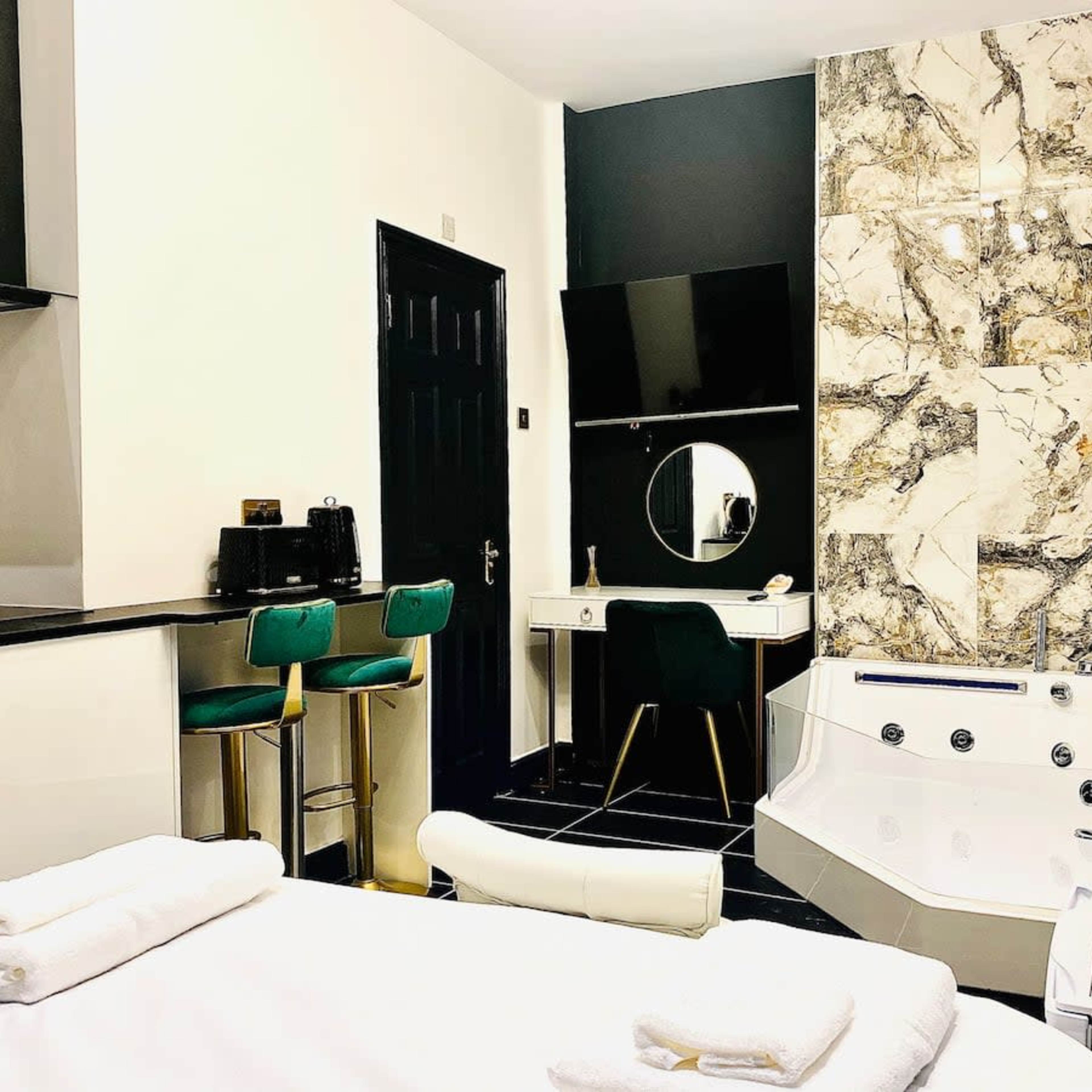 A modern bathroom featuring a large jacuzzi tub, a sleek vanity with a round mirror, and a small kitchenette area with bar stools.