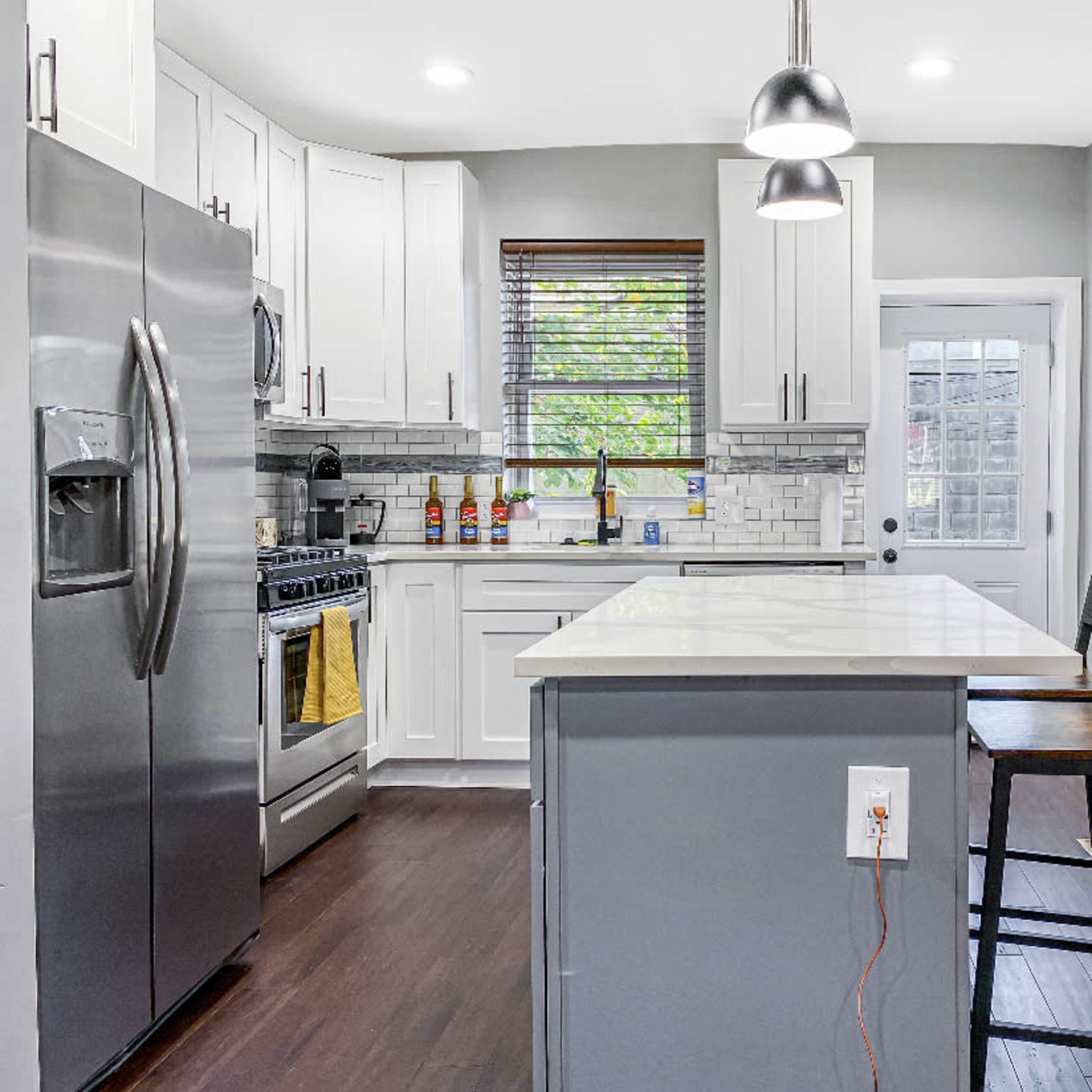 A modern kitchen features stainless steel appliances, white cabinetry, and a central island with bar stools.