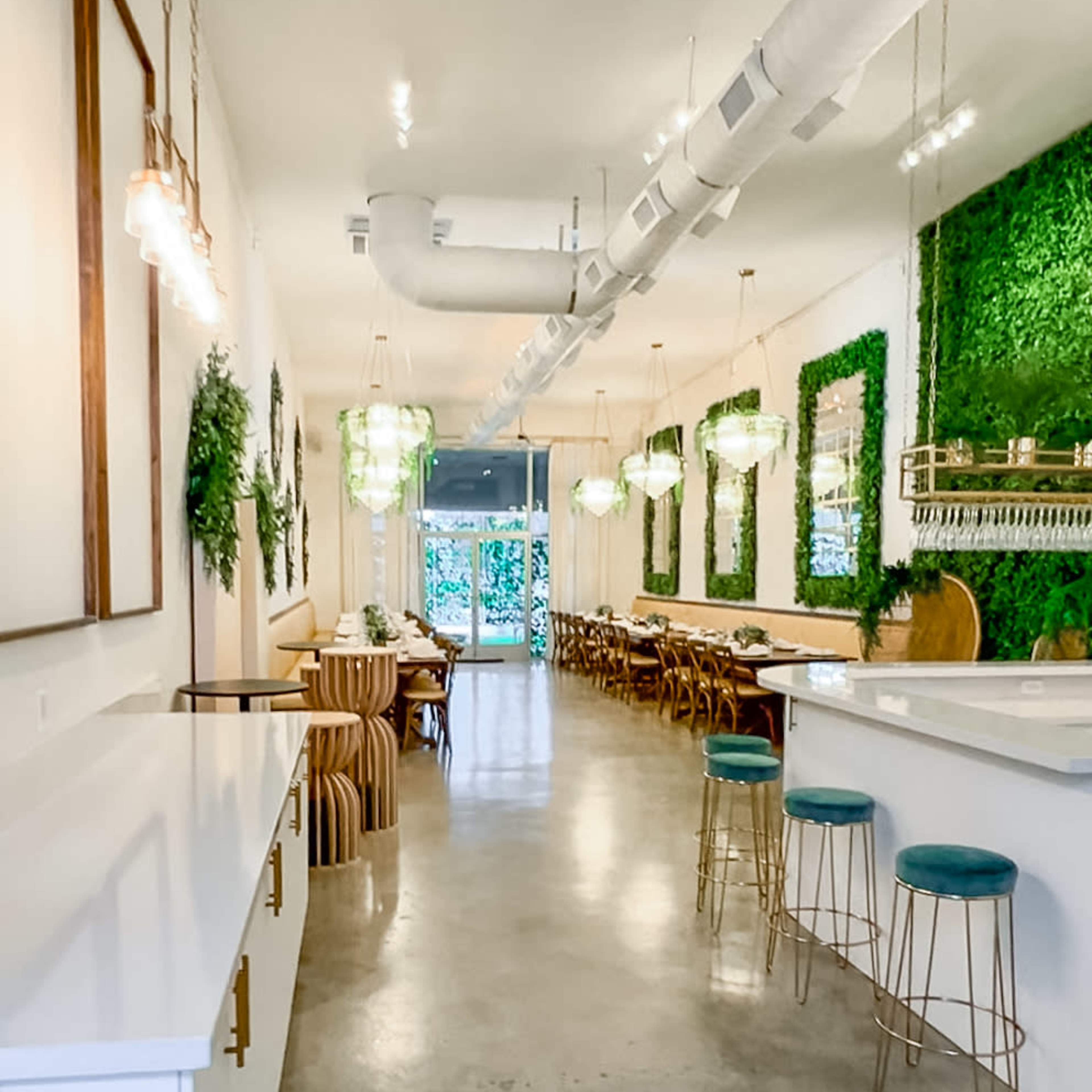 A modern restaurant interior with a concrete floor, green wall decor, and a mix of seating arrangements, including bar stools and wooden chairs.