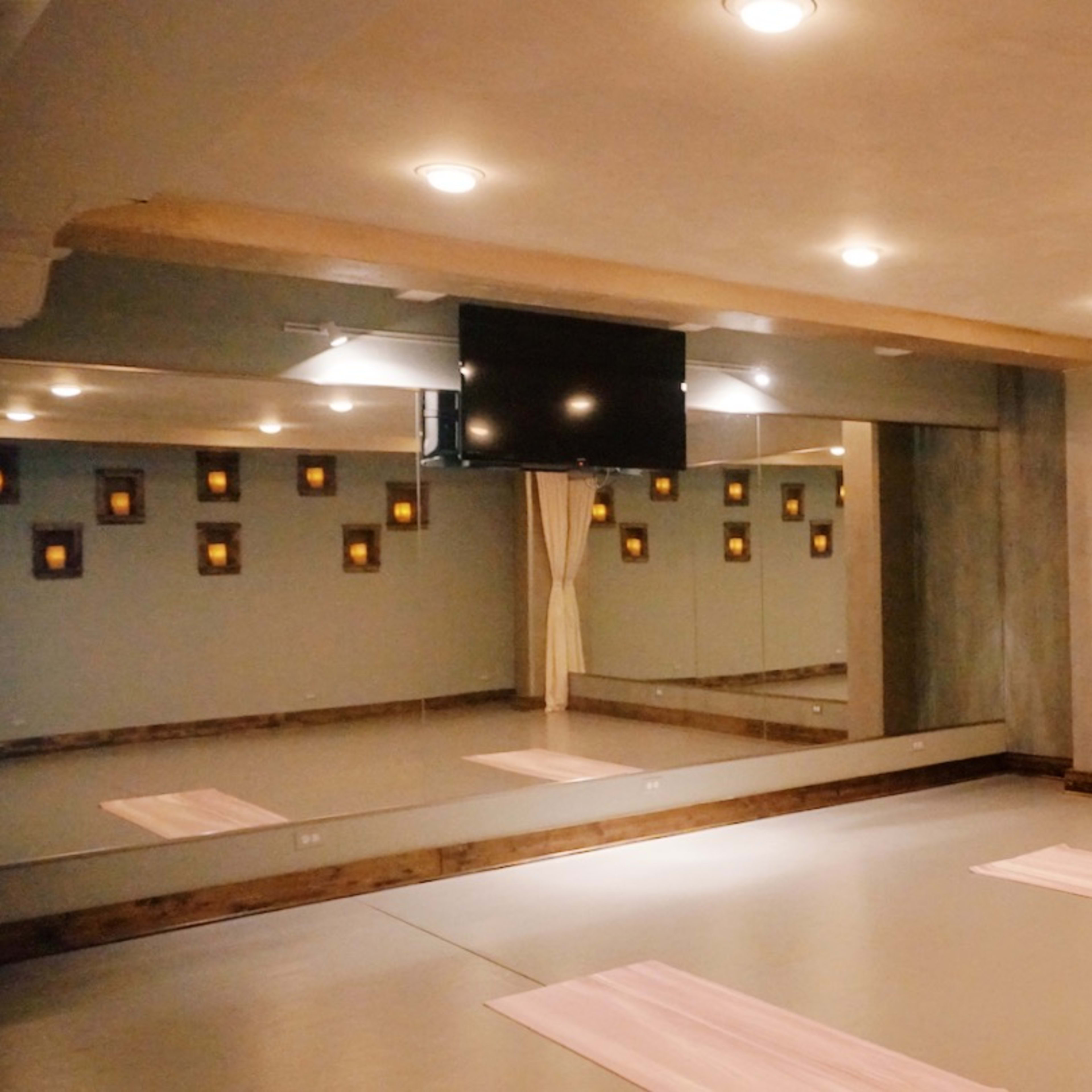 A spacious yoga studio with mirrors on one wall, soft lighting, and two pink mats laid out on the floor.