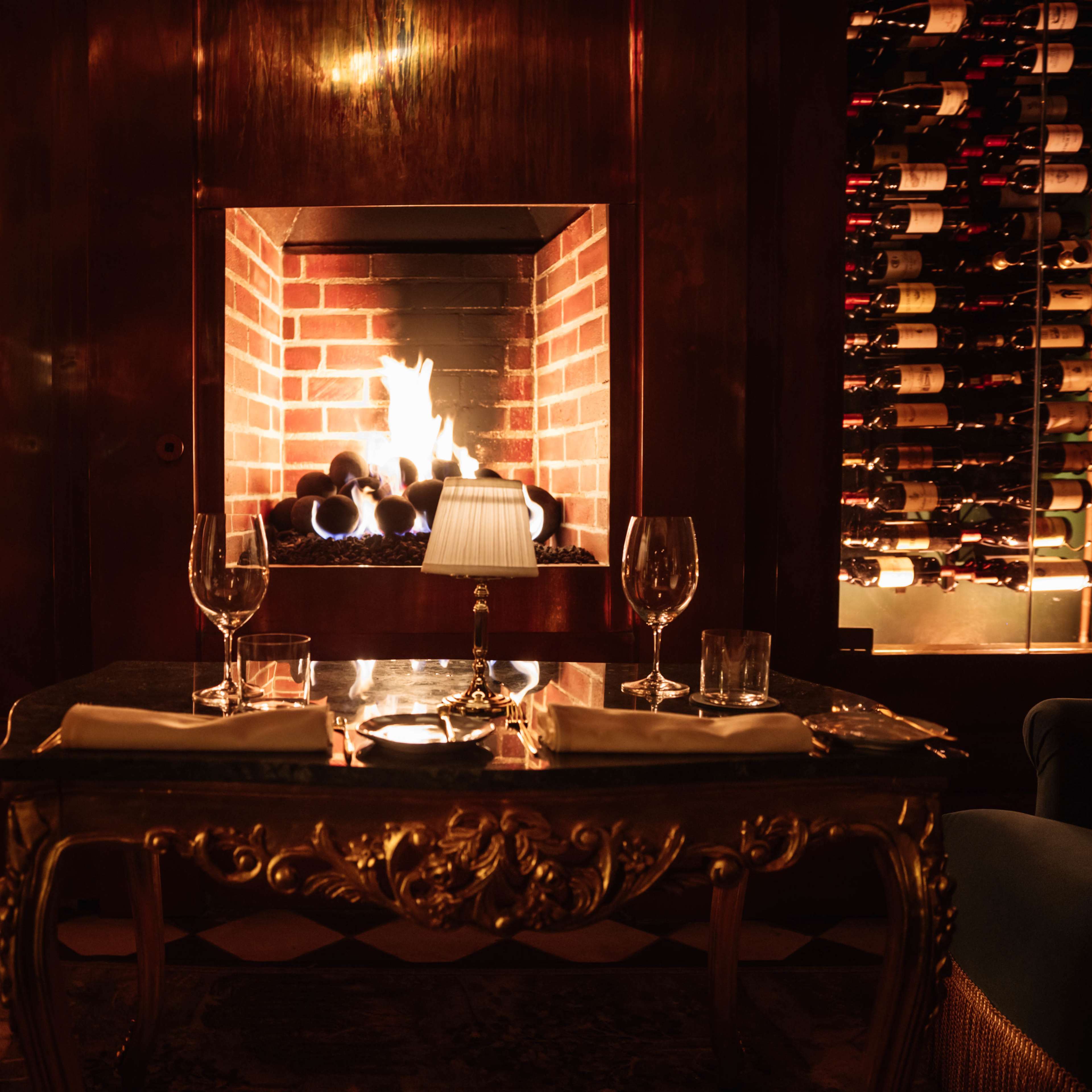 A dining area features a cozy fireplace surrounded by wine racks, and a table set with glassware.
