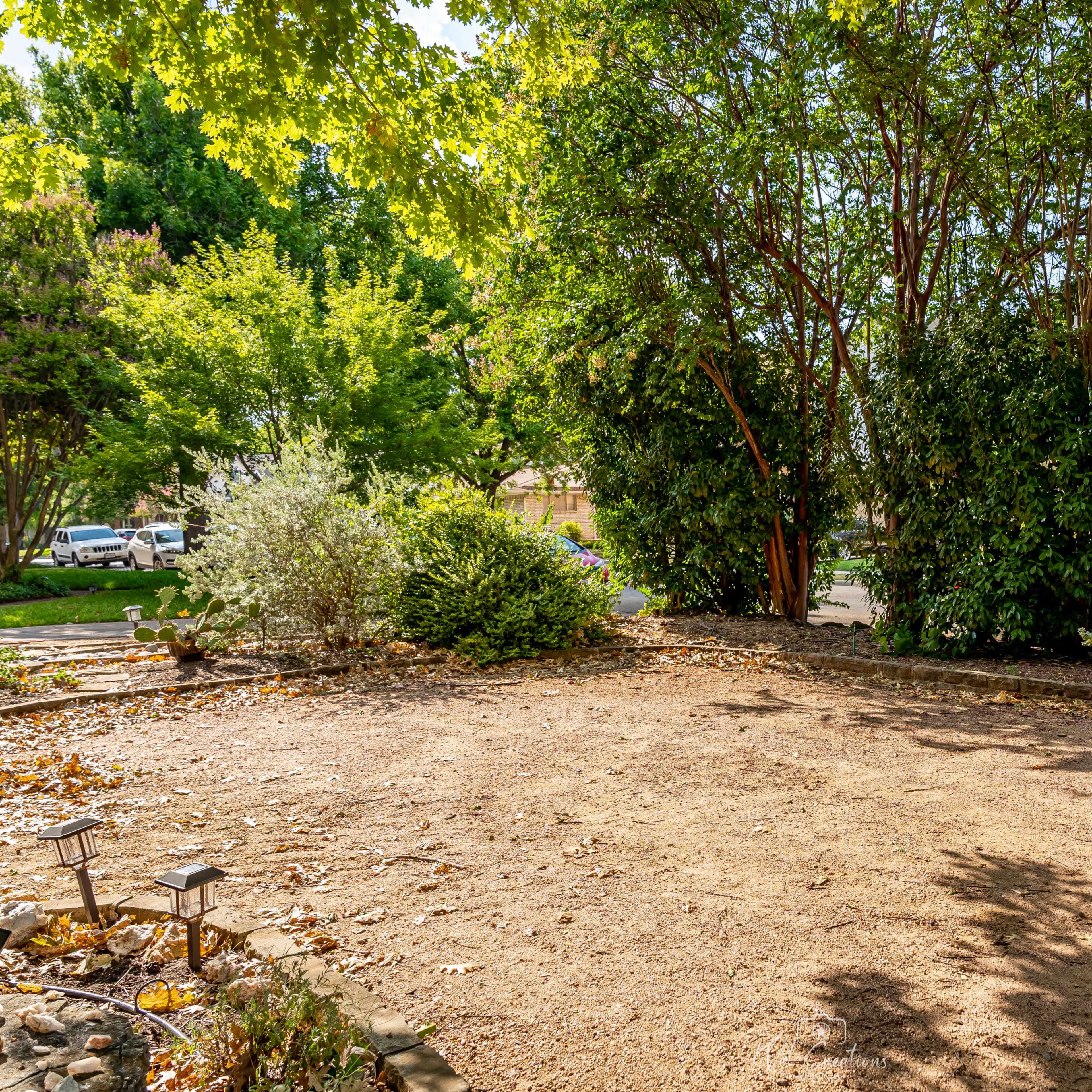 A cleared, sandy area surrounded by trees and shrubs, with a residential street visible in the background.