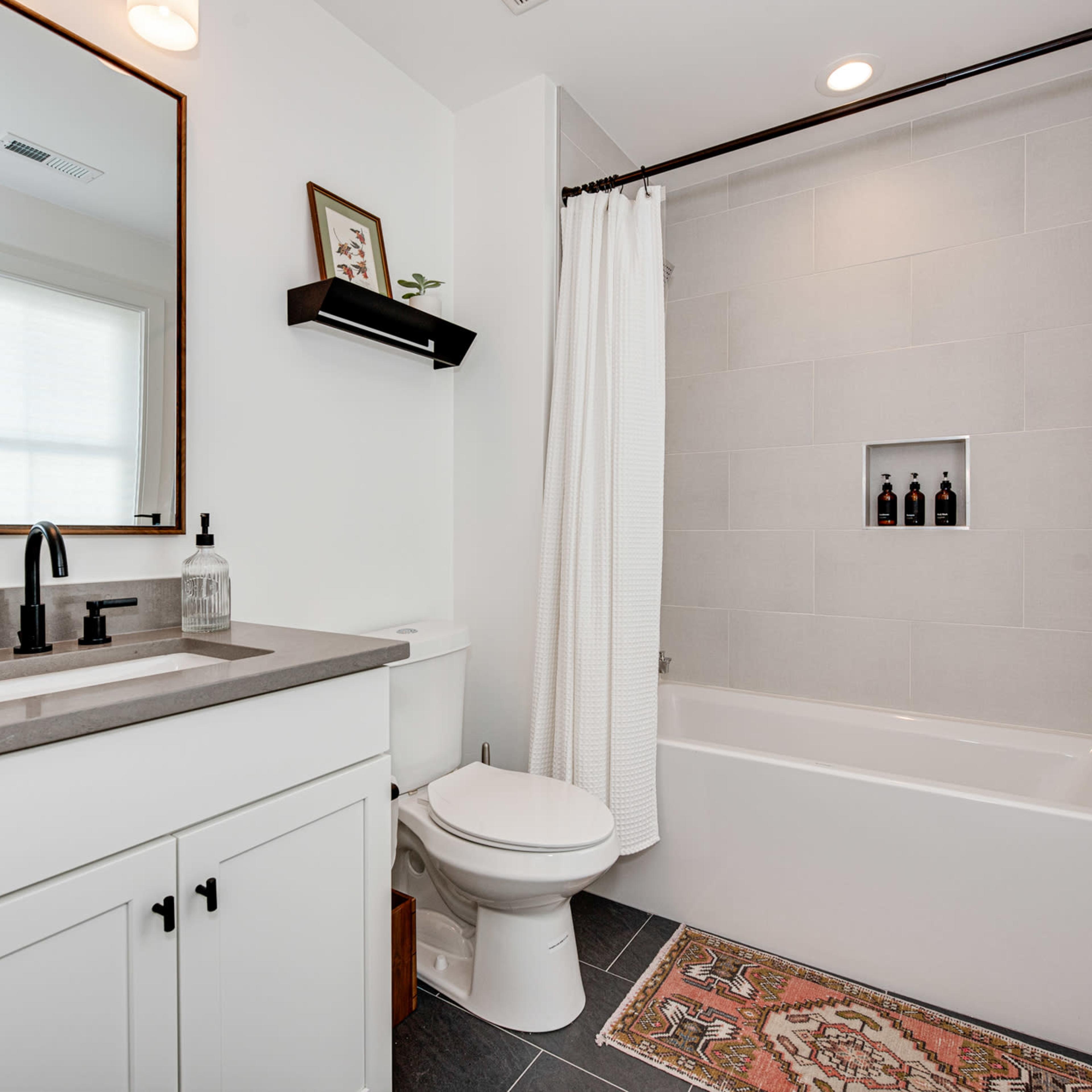 A modern bathroom featuring a sink with a countertop, a wall-mounted mirror, a toilet, and a bathtub with a shower curtain.