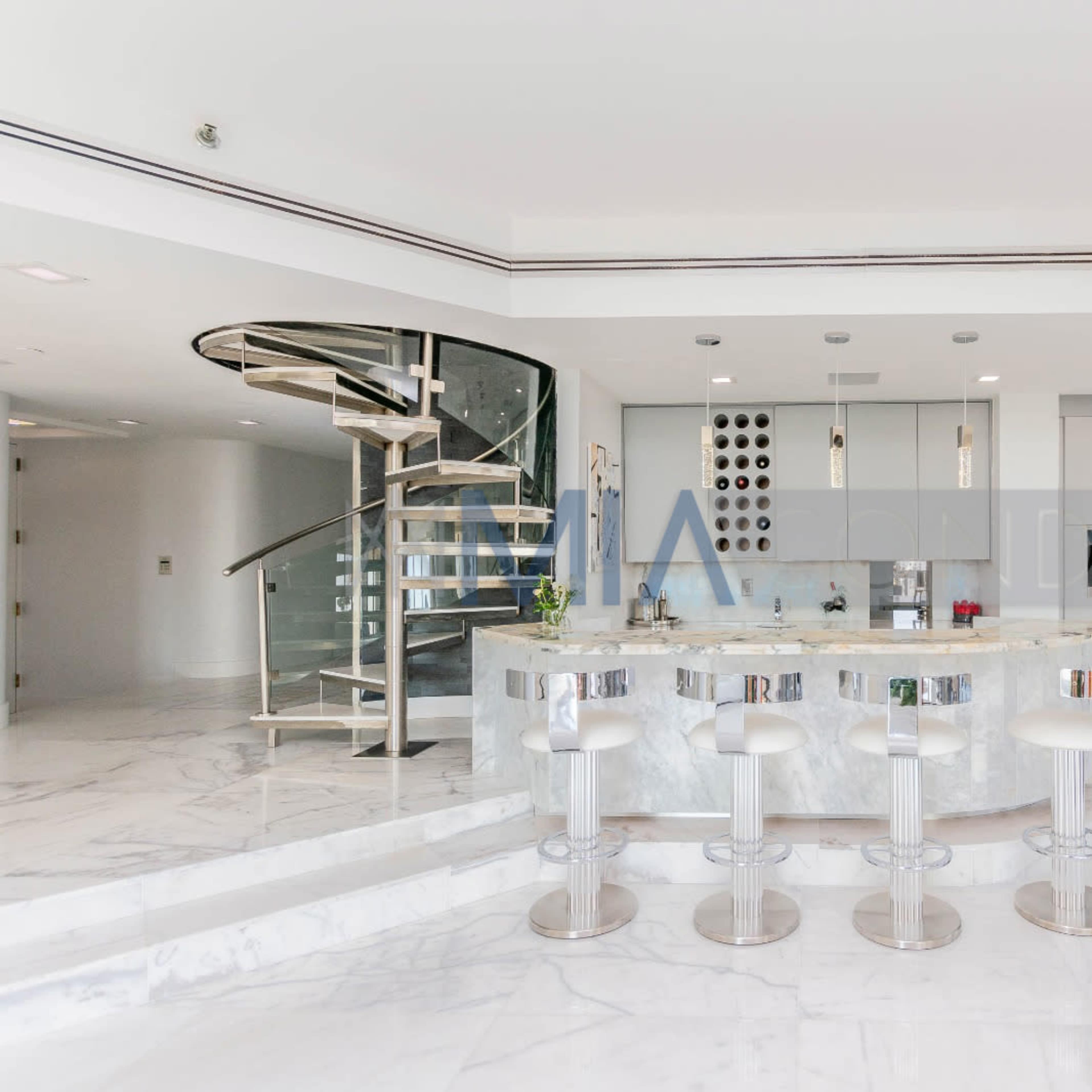 A modern kitchen with a spiral staircase, featuring a marble countertop and several sleek bar stools.