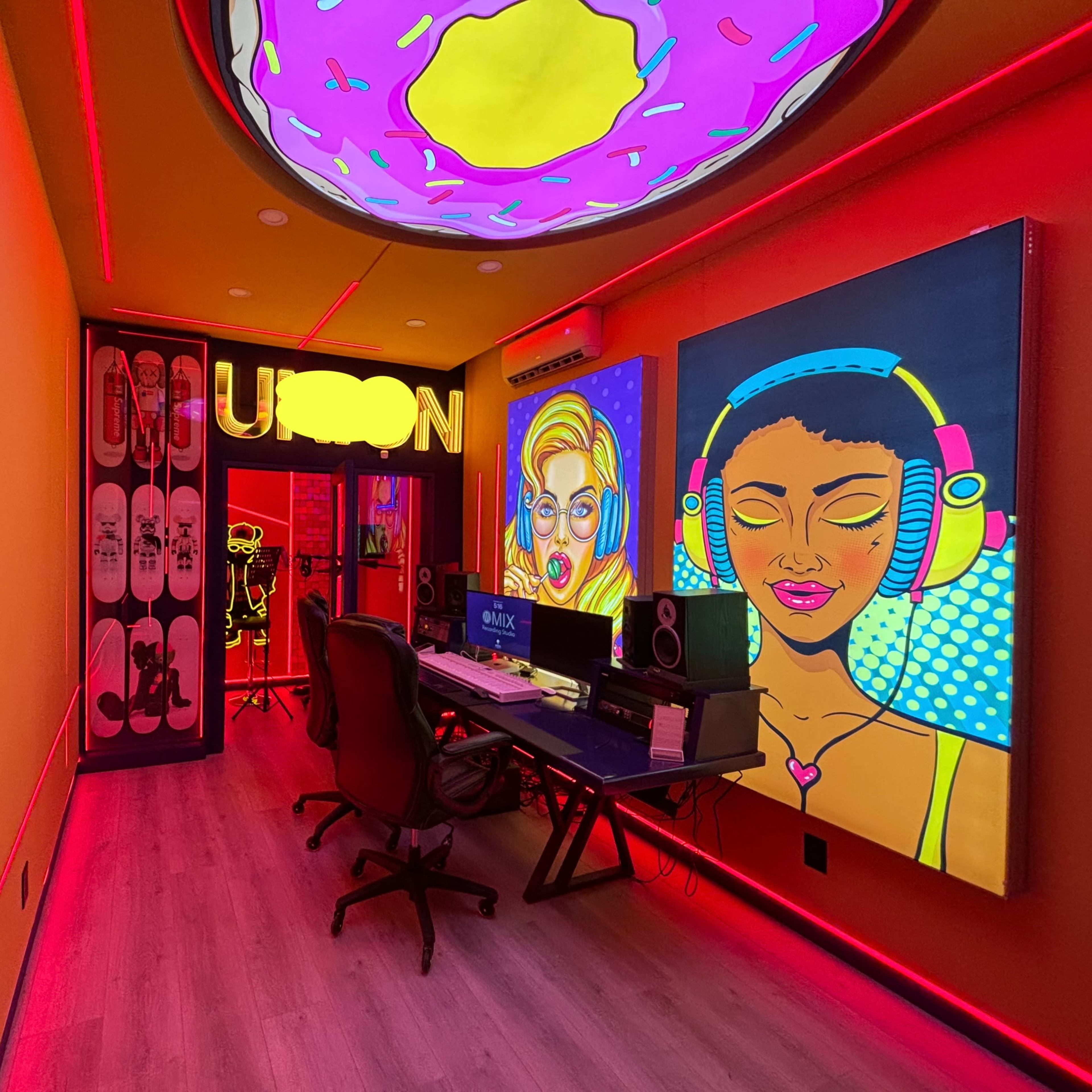 A brightly colored music studio featuring neon artwork, a desk with speakers, and skateboards mounted on the wall.