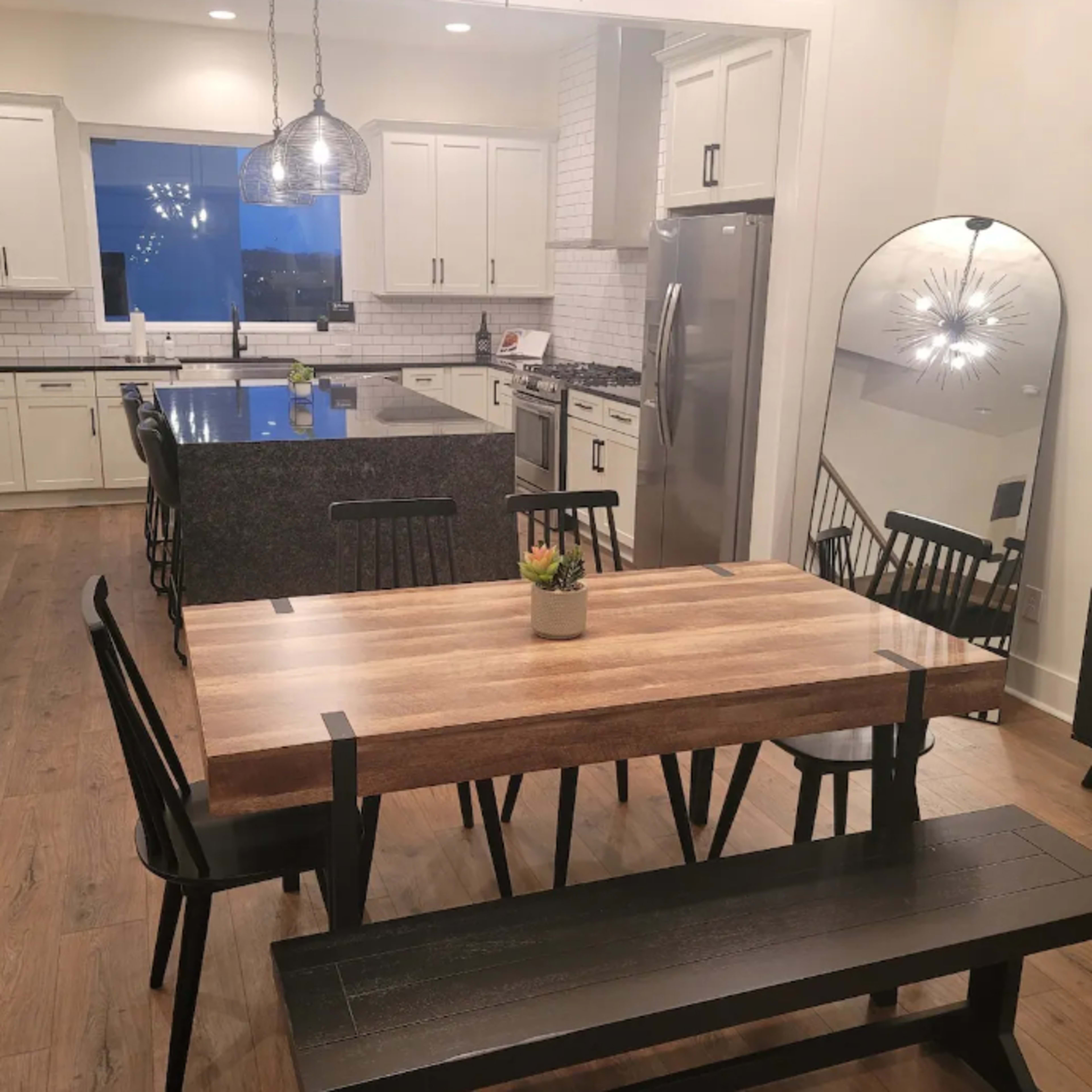 A modern kitchen and dining area feature a wooden dining table with black chairs, a large island with a dark countertop, and sleek cabinetry.